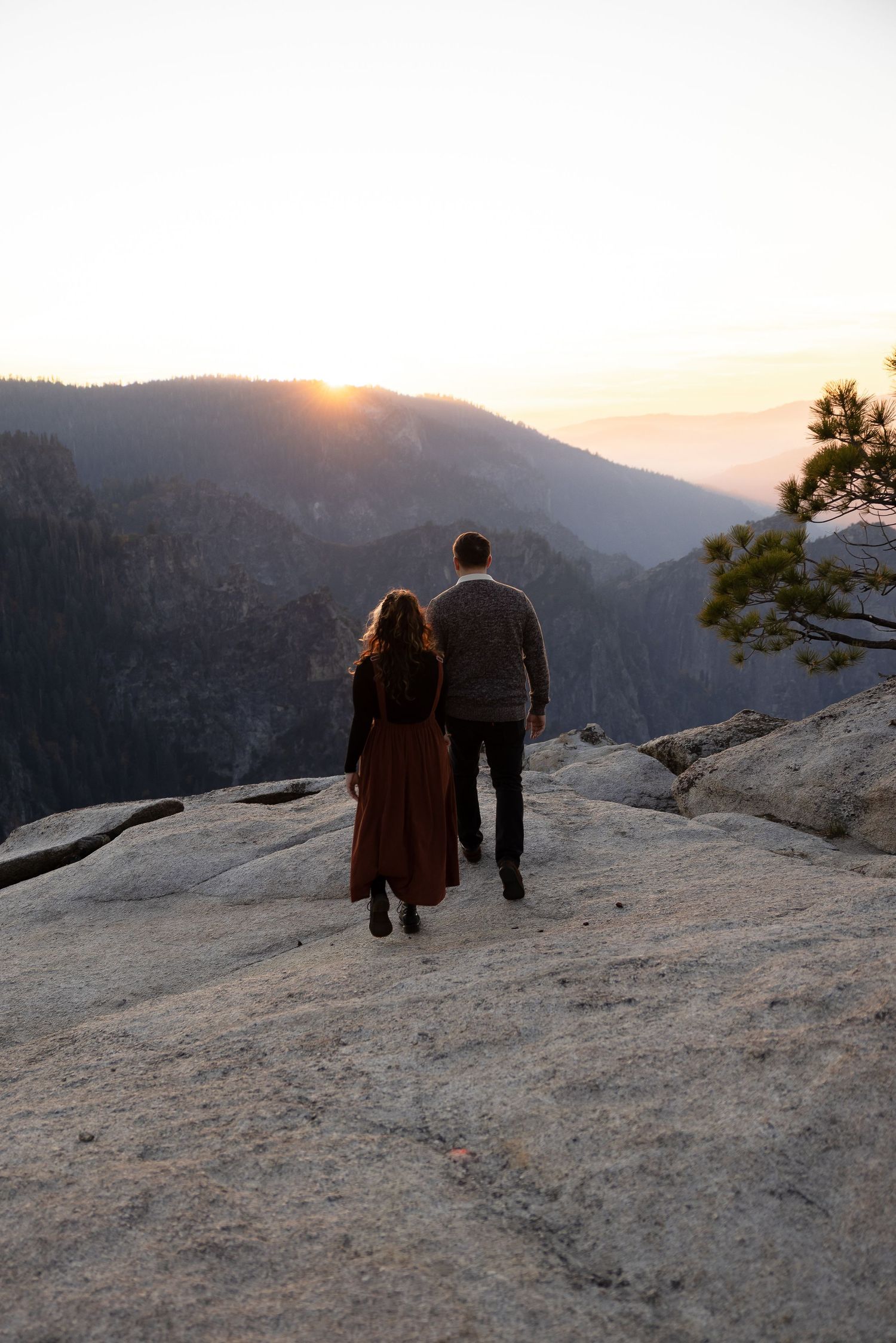 Two figures walk together along a rocky mountain ridge at sunset.