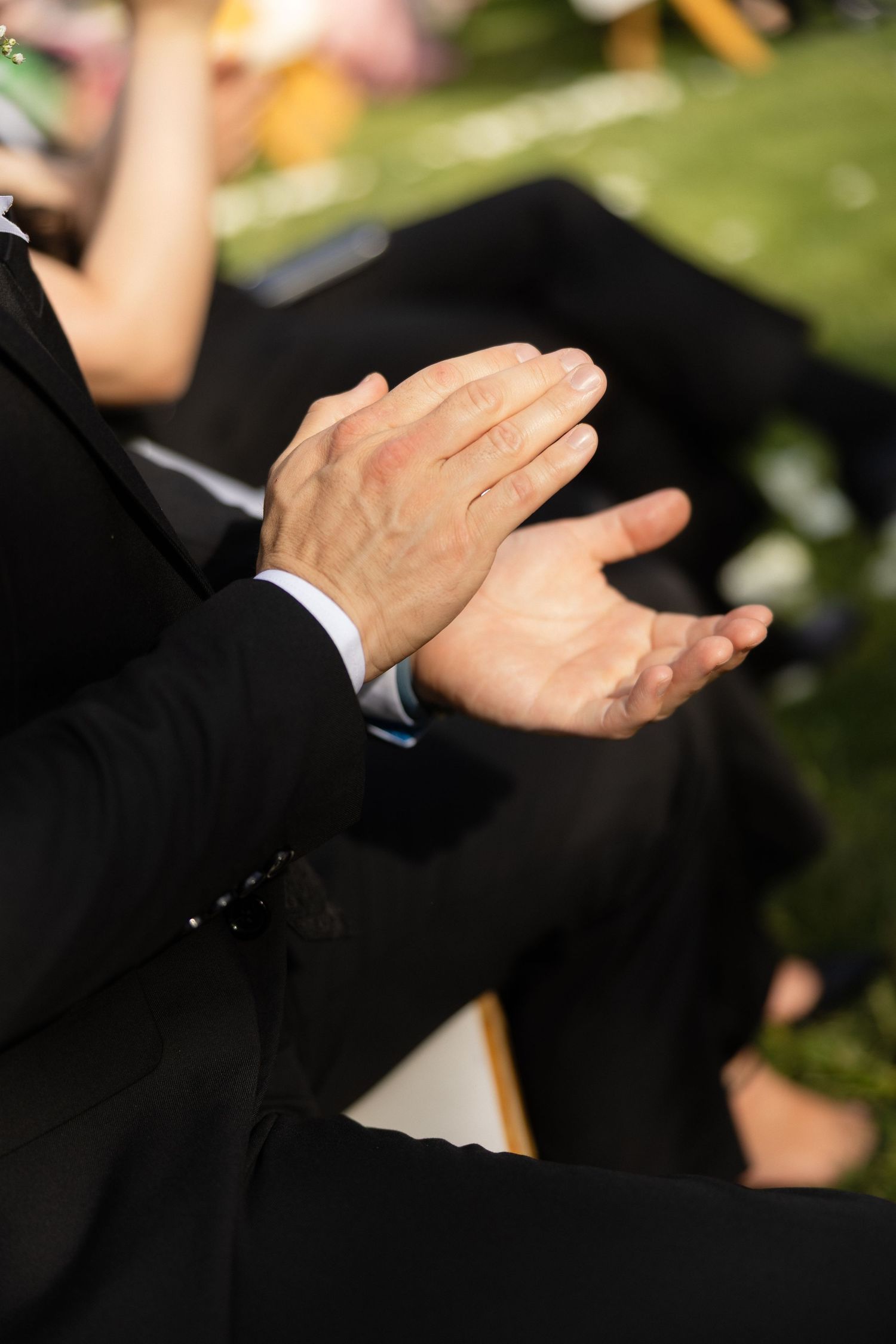 Wedding guests in formal attire clapping hands during outdoor ceremony celebration.