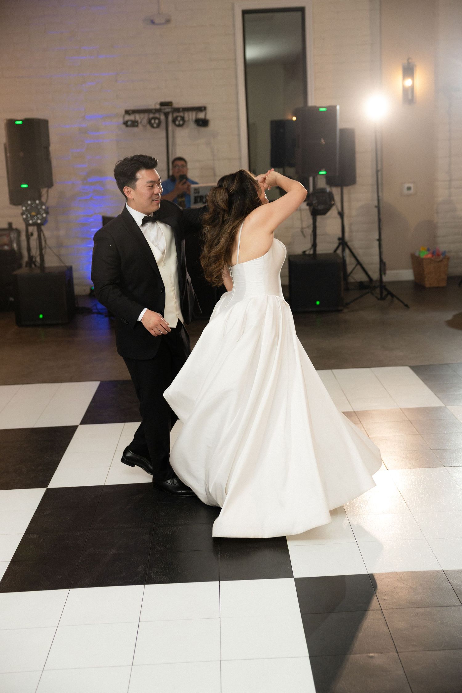 Bride in white ball gown and groom in tuxedo sharing first dance on checkered floor.