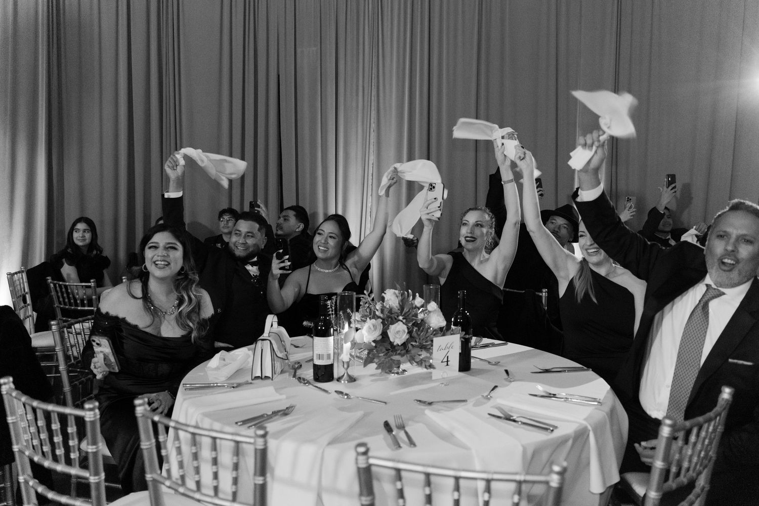 Black and white photo of wedding guests waving napkins during a reception celebration.