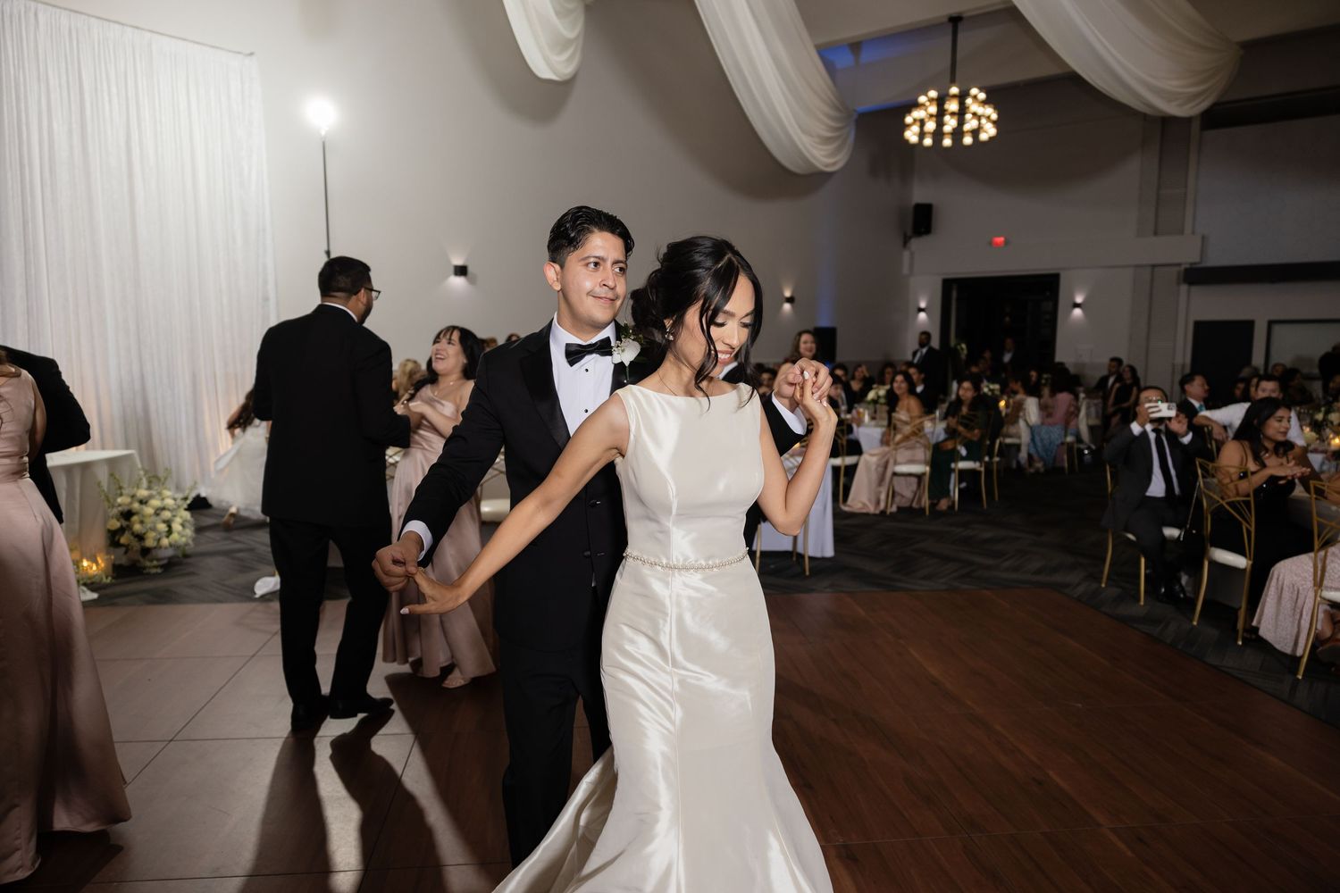 Wedding celebration in progress with couples dancing on wooden floor beneath elegant white draping.