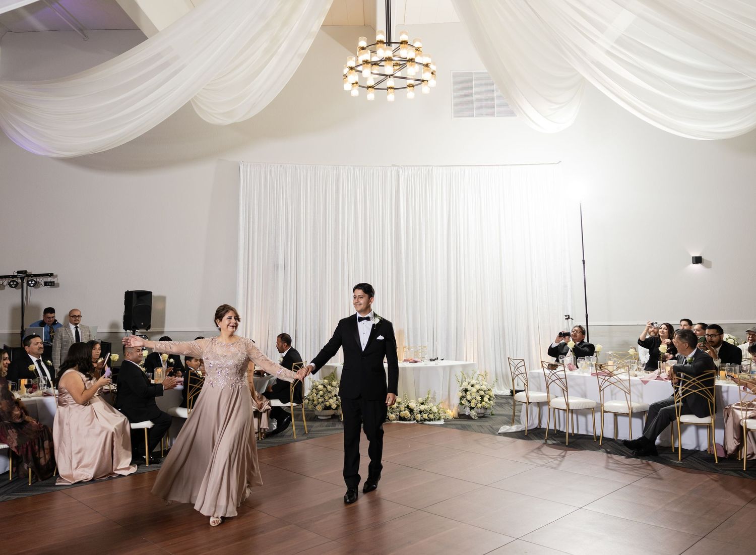 Elegant wedding venue with draped ceiling and chandelier lighting during reception.