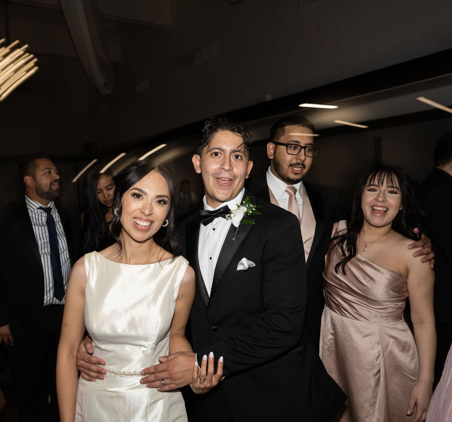 Wedding party members pose together in formal attire at an evening celebration.