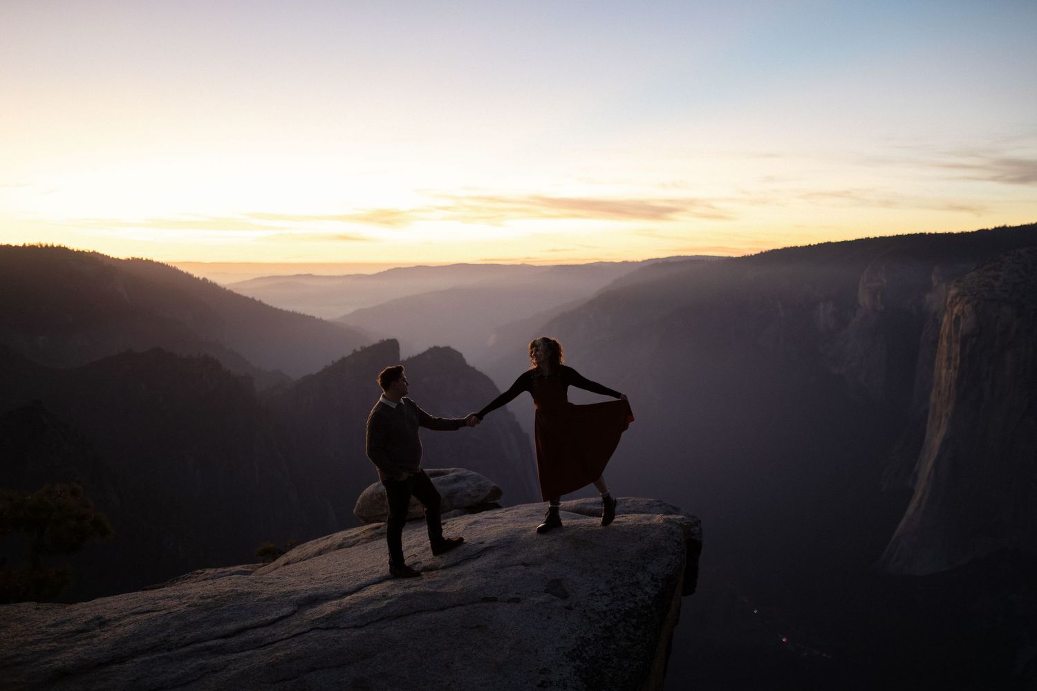 Silhouetted figures on mountain cliff edge during golden hour in Yosemite National Park.