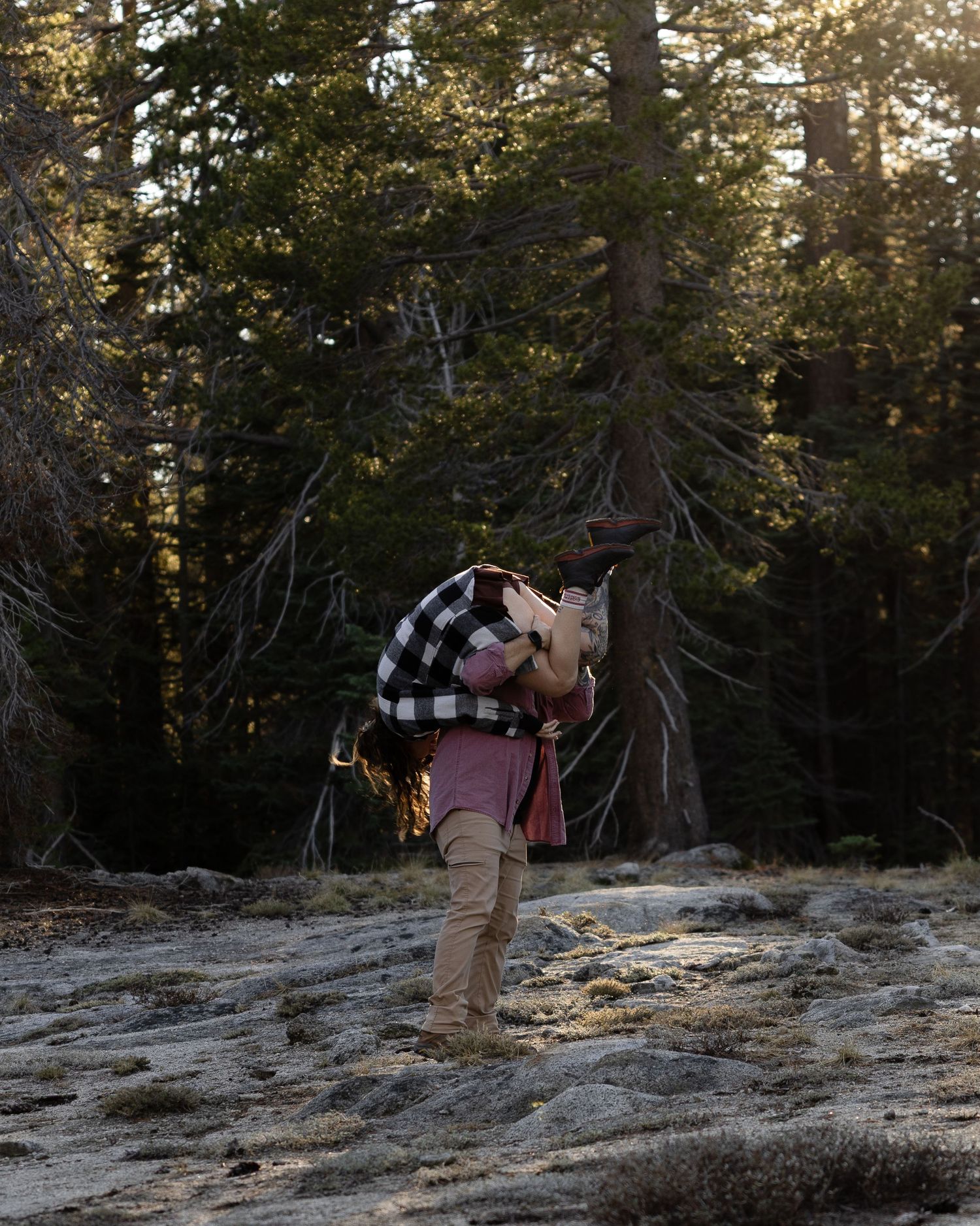 Two people exploring a rocky mountain trail surrounded by evergreen trees at golden hour.