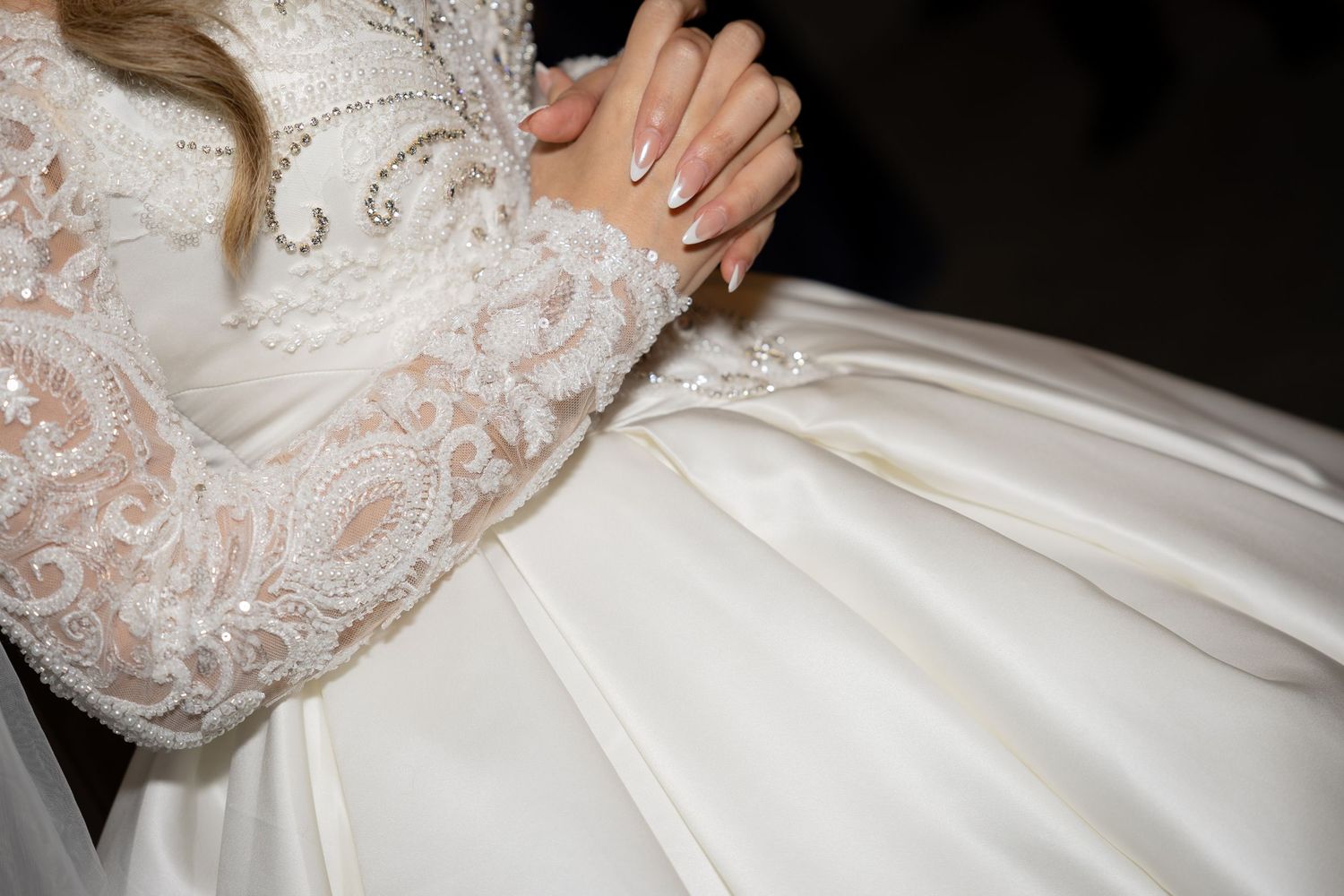 Close-up detail of intricate lace sleeves and pleated fabric on a white wedding gown.
