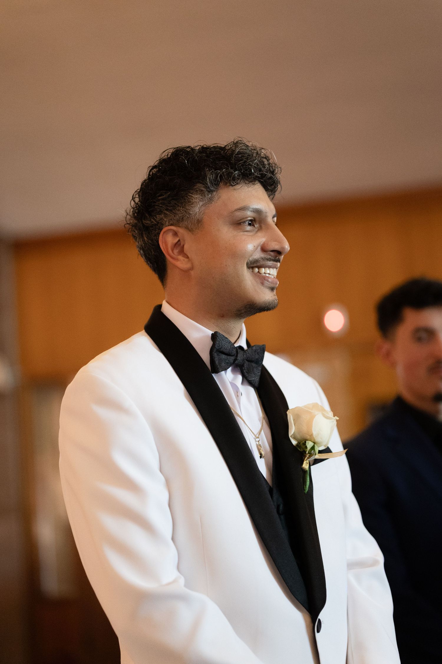 Wedding party member in white tuxedo jacket and black bow tie smiling.