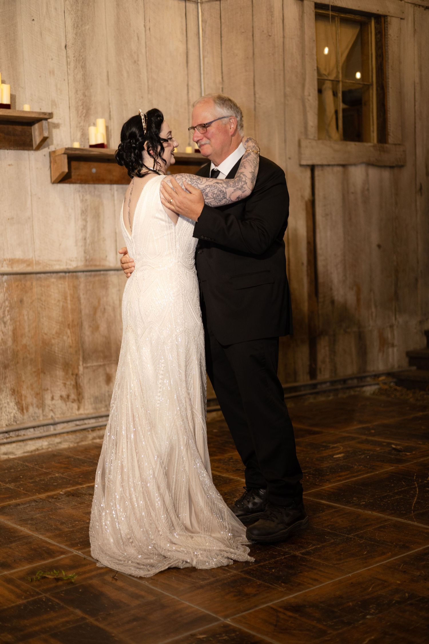 Dancing couple in formal attire twirl beneath warm lighting in a rustic indoor setting.