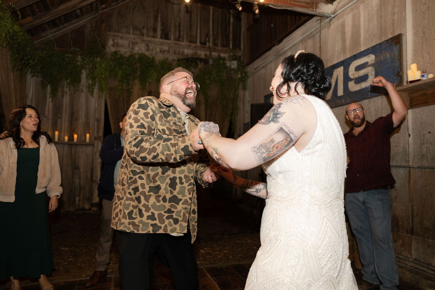 Wedding party dances beneath string lights in a converted barn space with rustic decor.