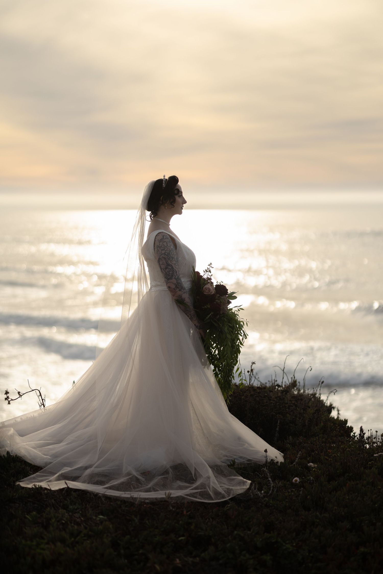 Dramatic silhouette of bride in flowing gown against sunset ocean waves.