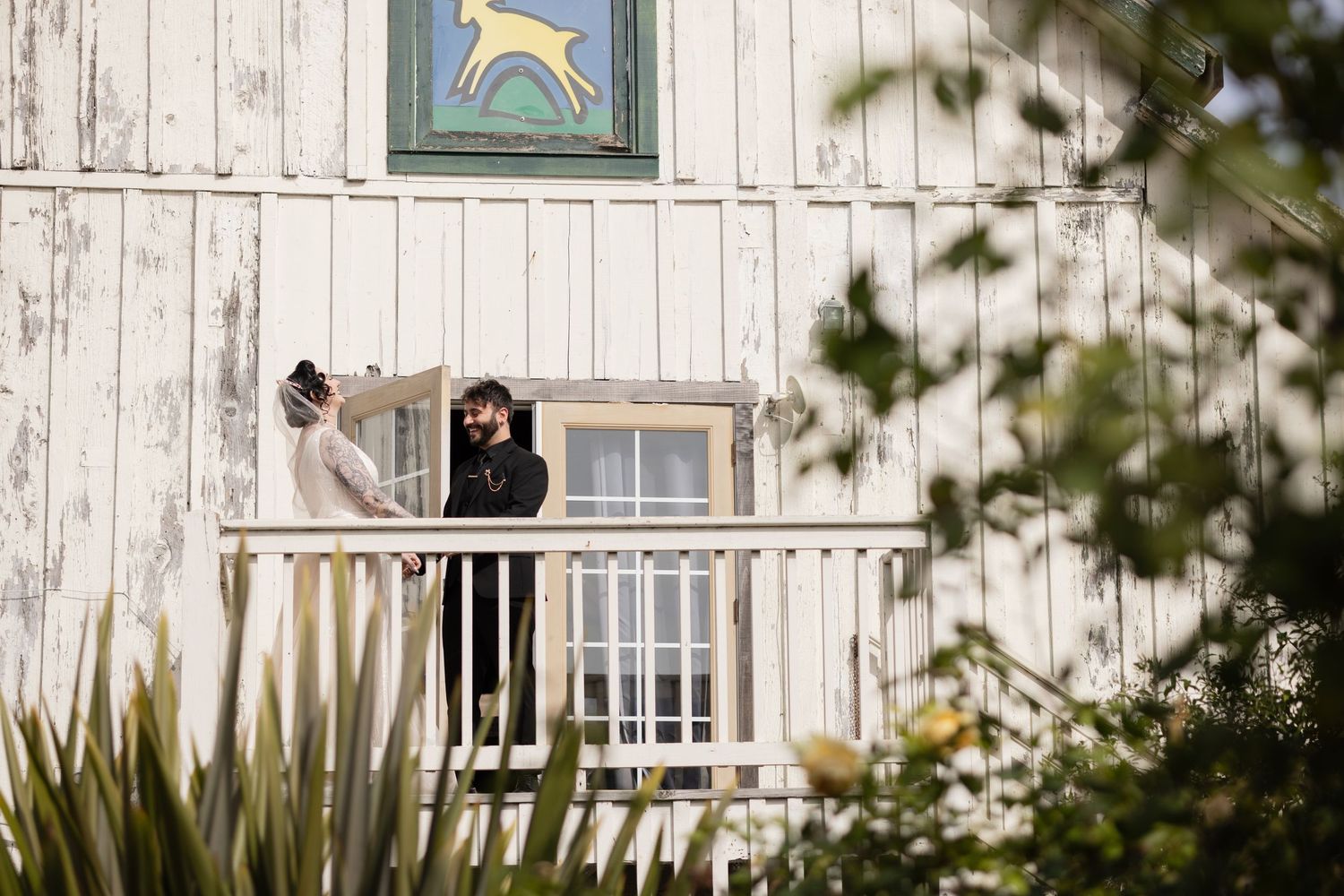 A couple shares a moment on a white barn's balcony with a whimsical deer design above.