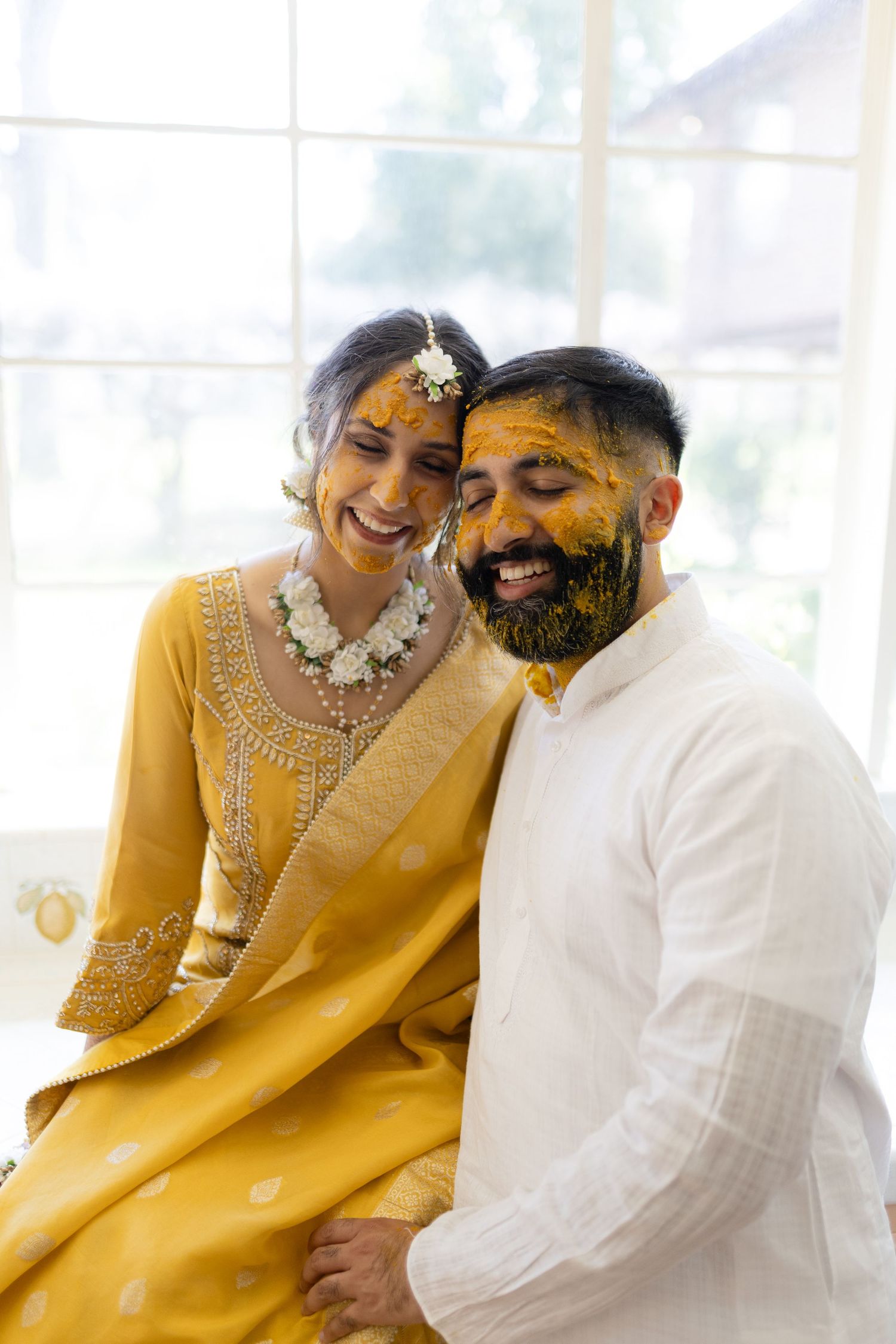 A couple in traditional Indian attire share joyful moments in a bright yellow and white themed photoshoot.