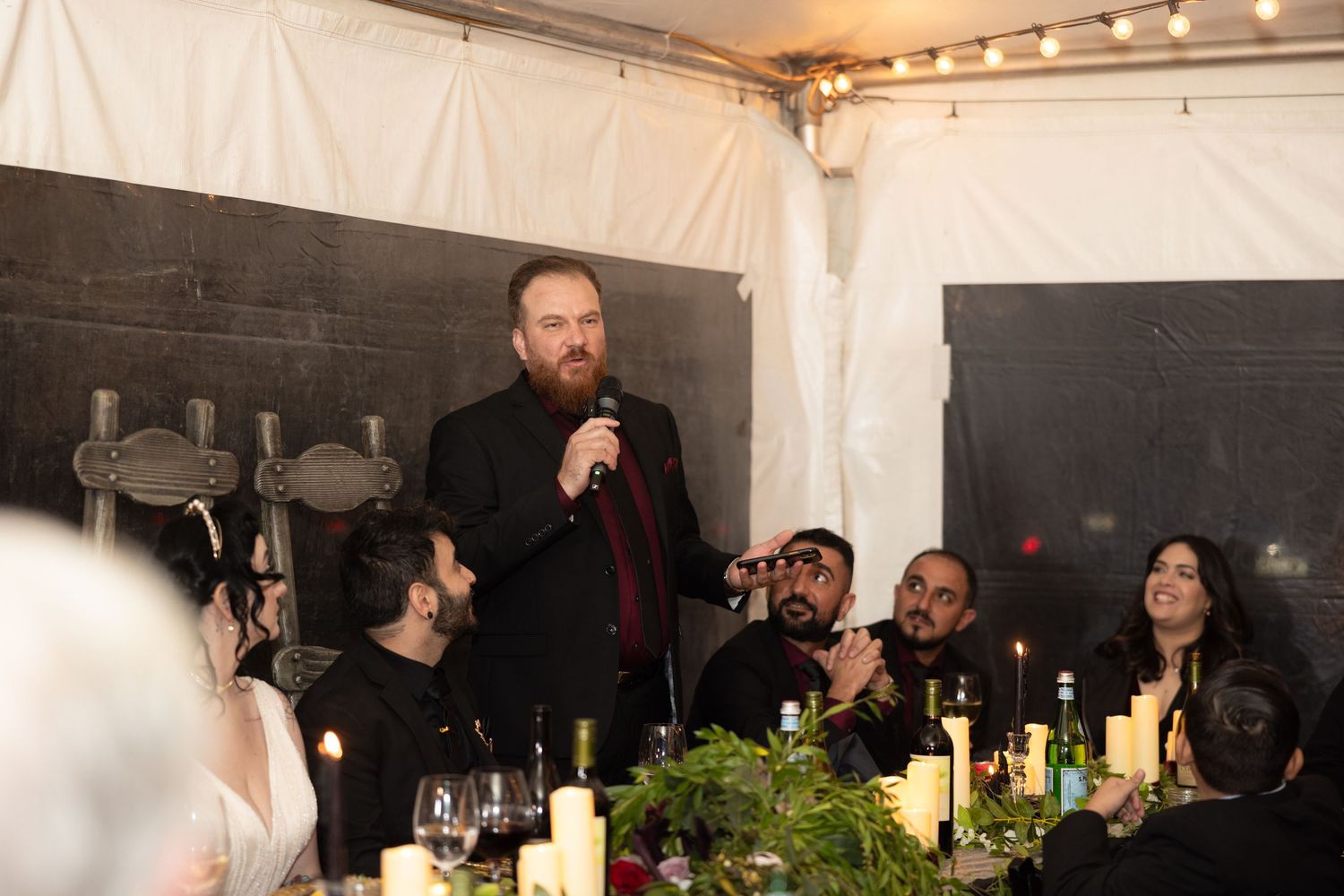 Indoor reception venue with string lights and guests seated at long dining tables.