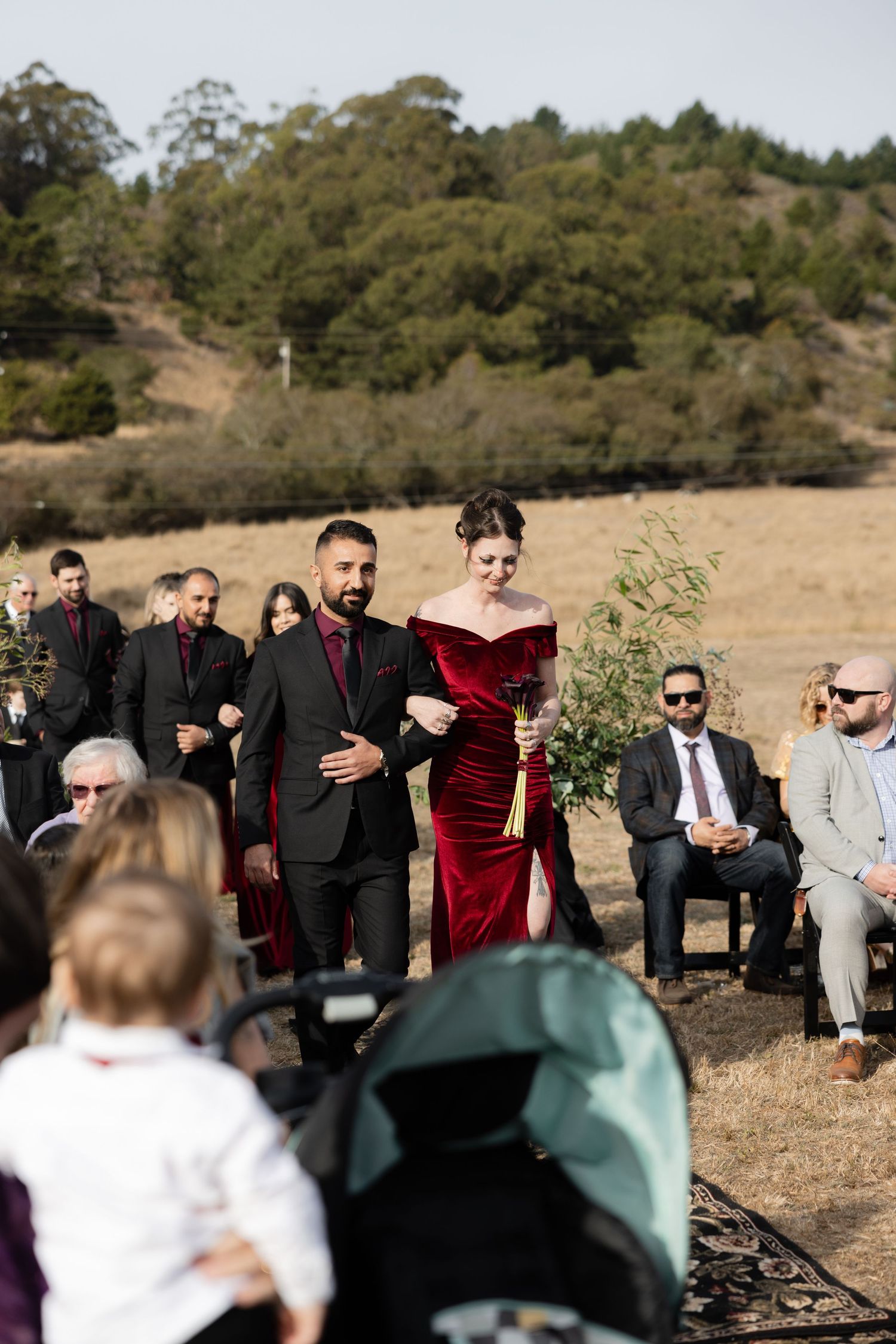 Wedding guests seated outdoors in formal attire against a natural landscape.