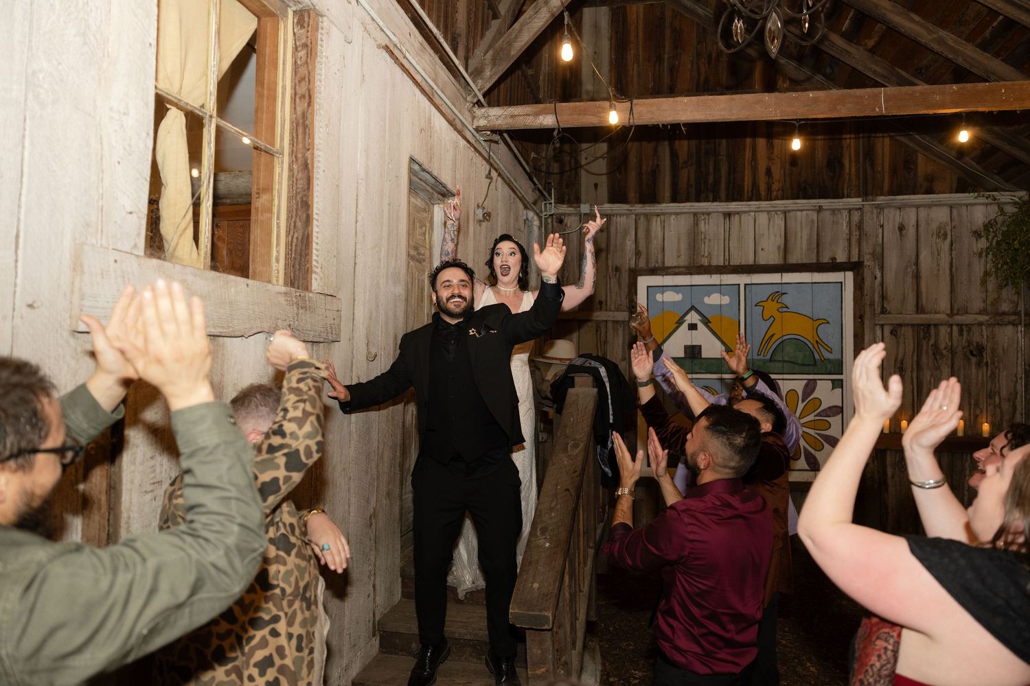 Wedding celebration with guests raising hands in joy inside rustic wooden barn venue.