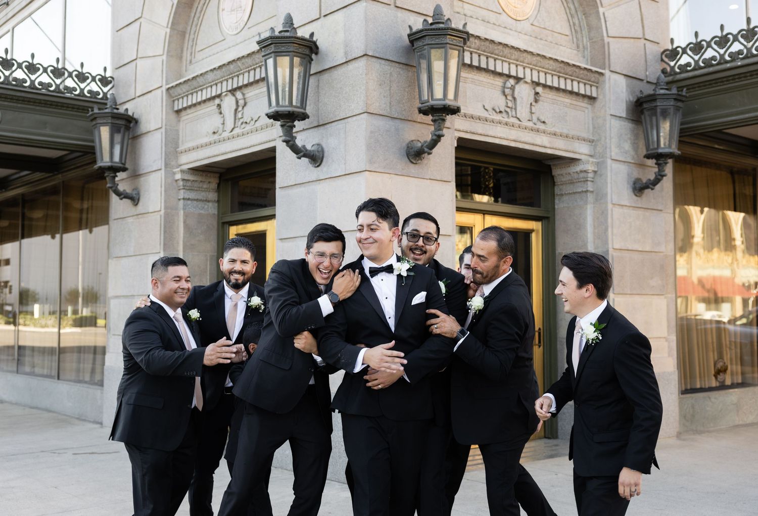 Wedding party members interacting casually outside historic stone venue.
