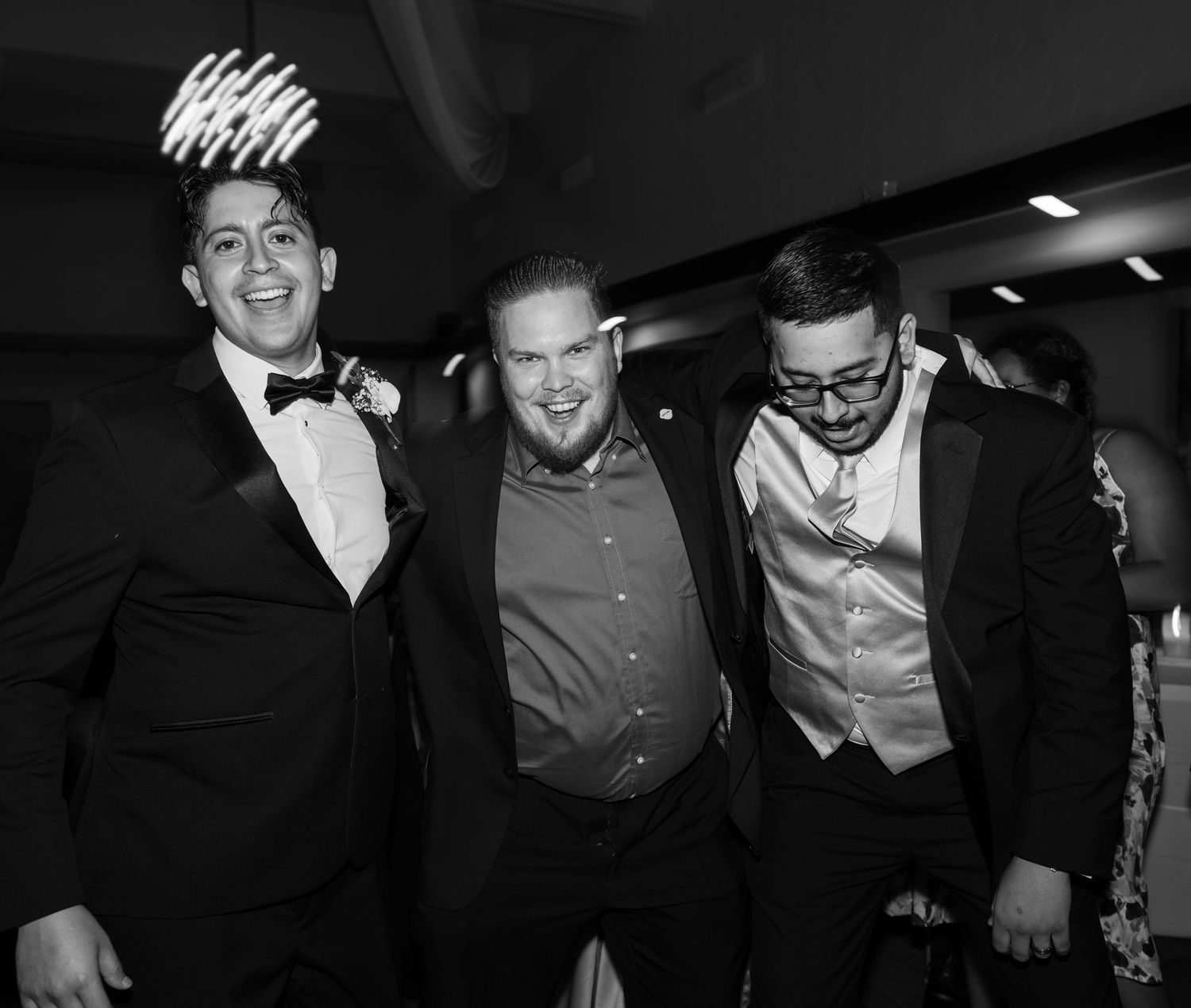 Three friends in formal attire laugh and pose together at an evening celebration.