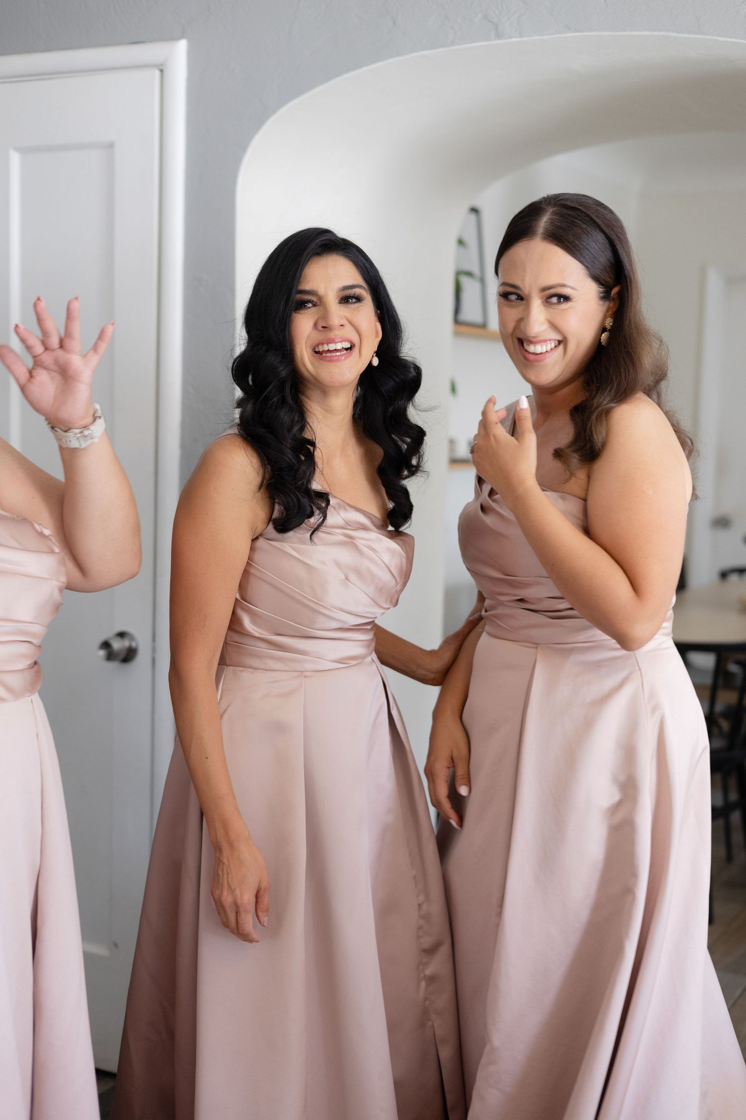 Bridesmaids in blush pink strapless dresses share a joyful moment together in a bright interior setting.