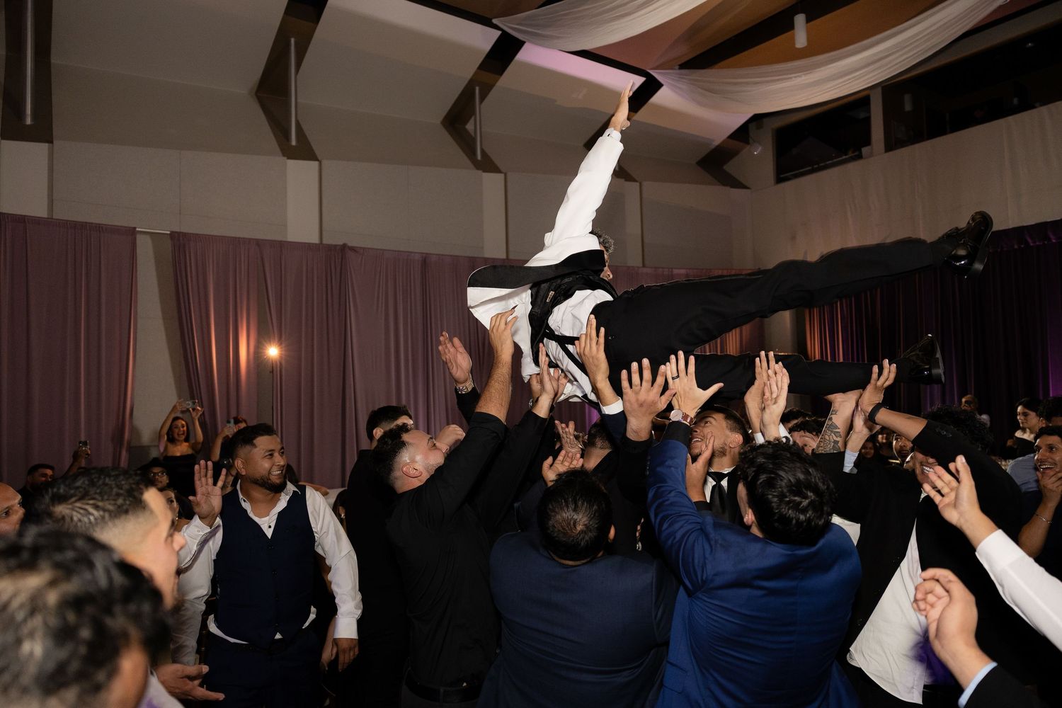 Wedding guests lift someone high into the air during an exciting reception celebration.
