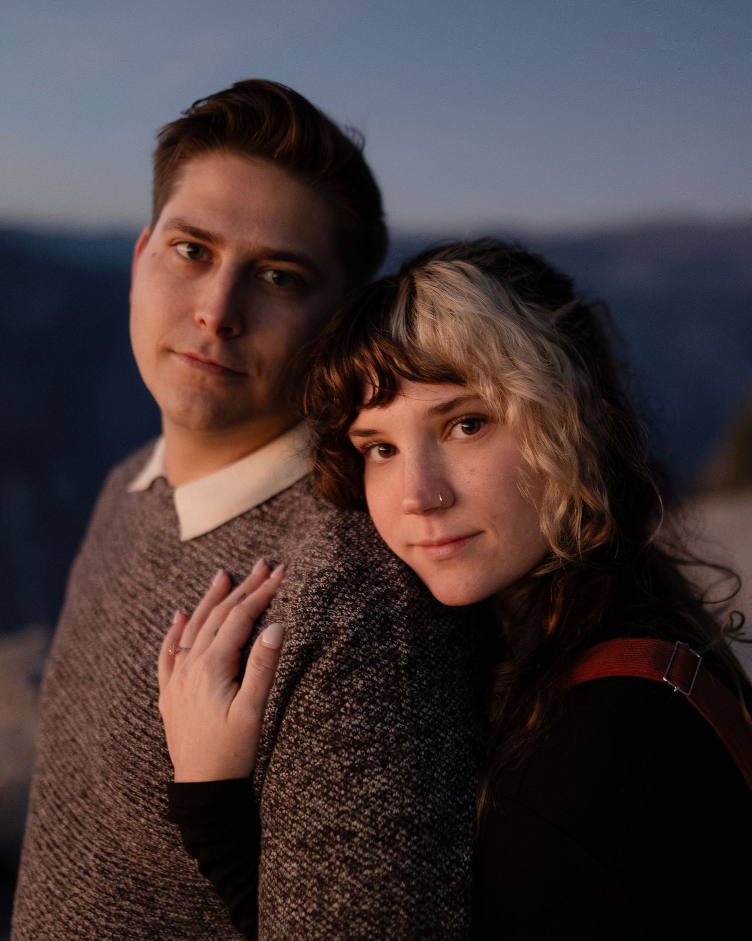 Couple in warm sweaters embrace during sunset in mountain landscape.