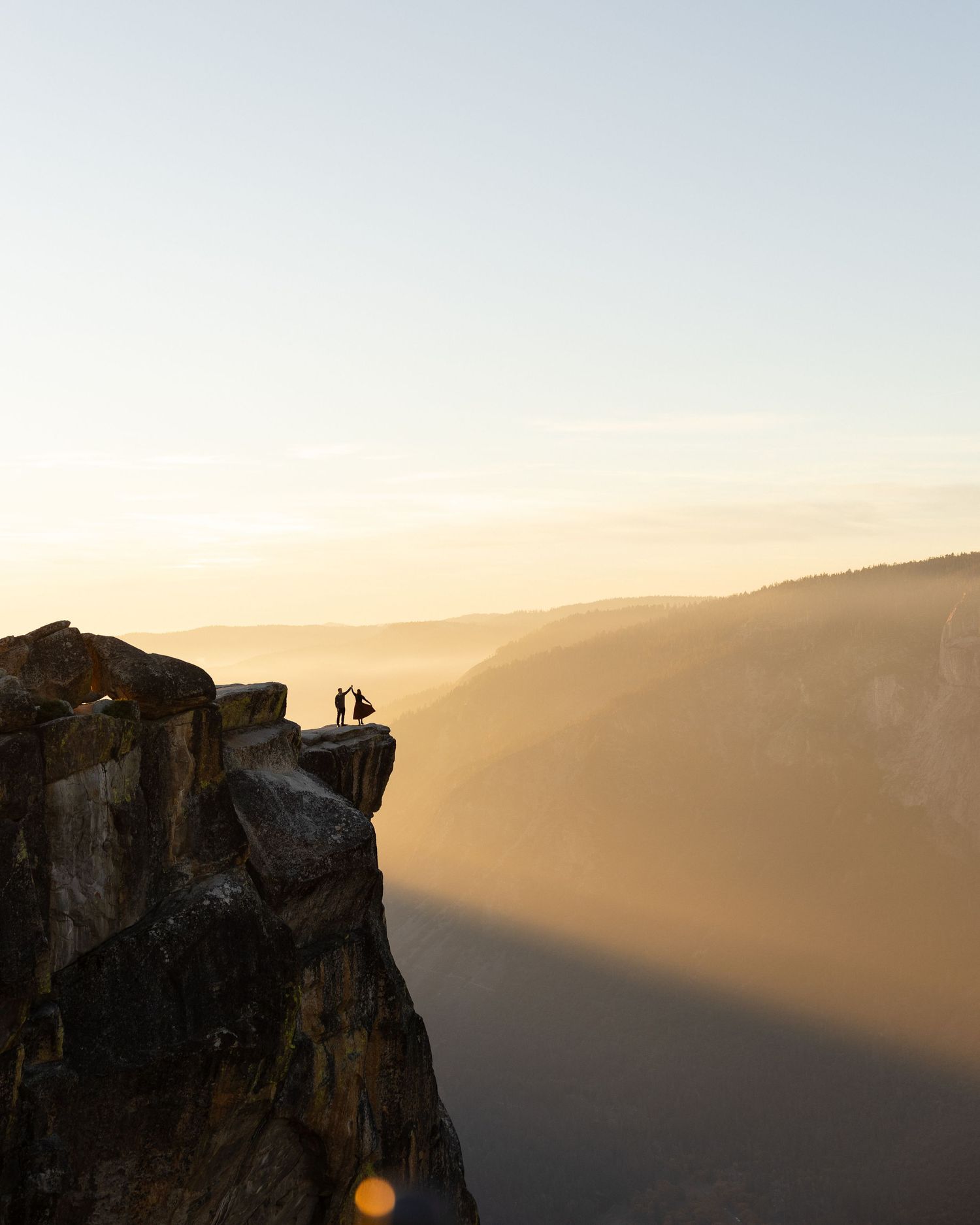 Small silhouettes on a majestic cliff edge during sunset in mountainous terrain.