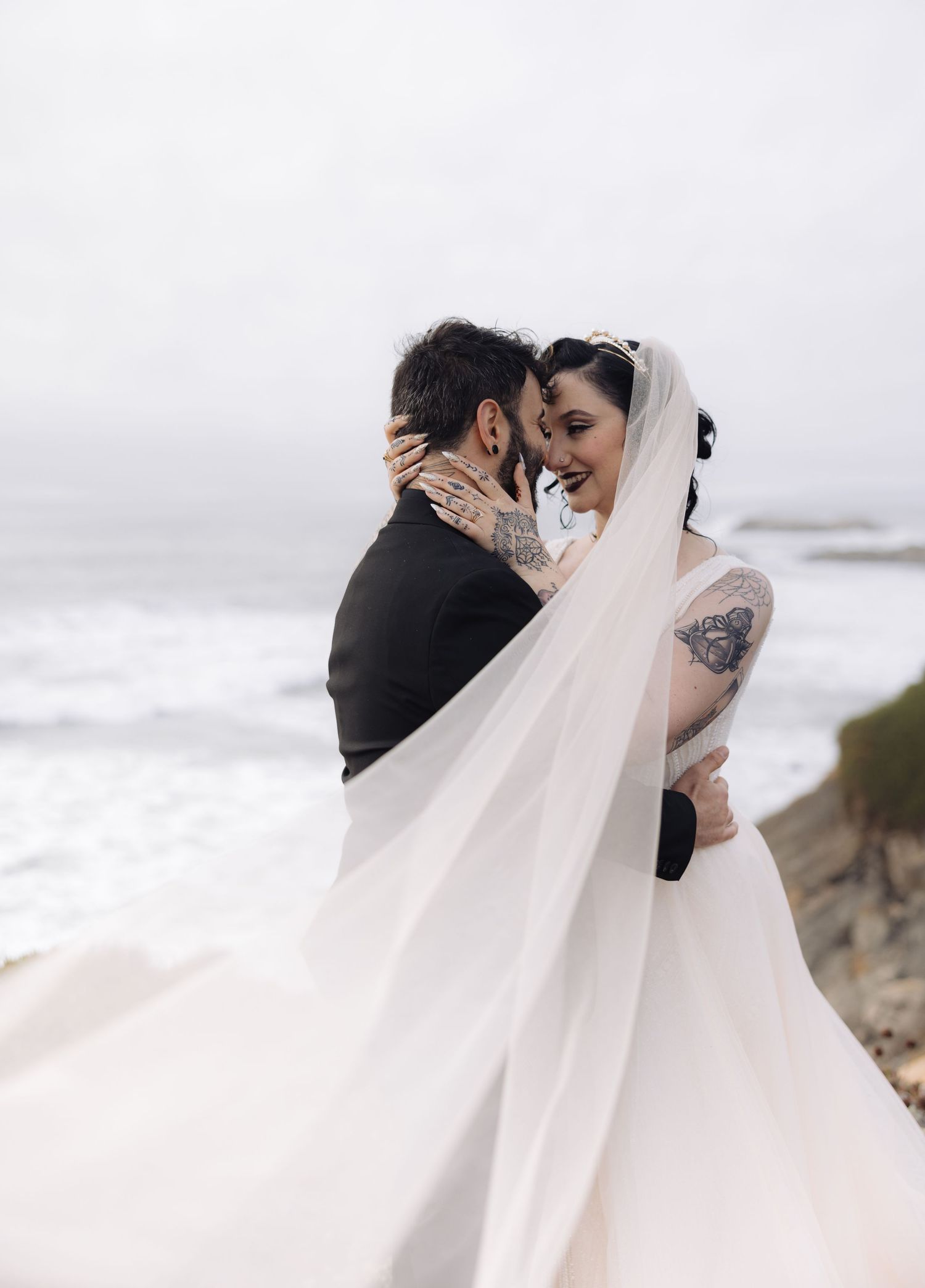 Intimate coastal wedding portrait with flowing veil against dramatic ocean backdrop.