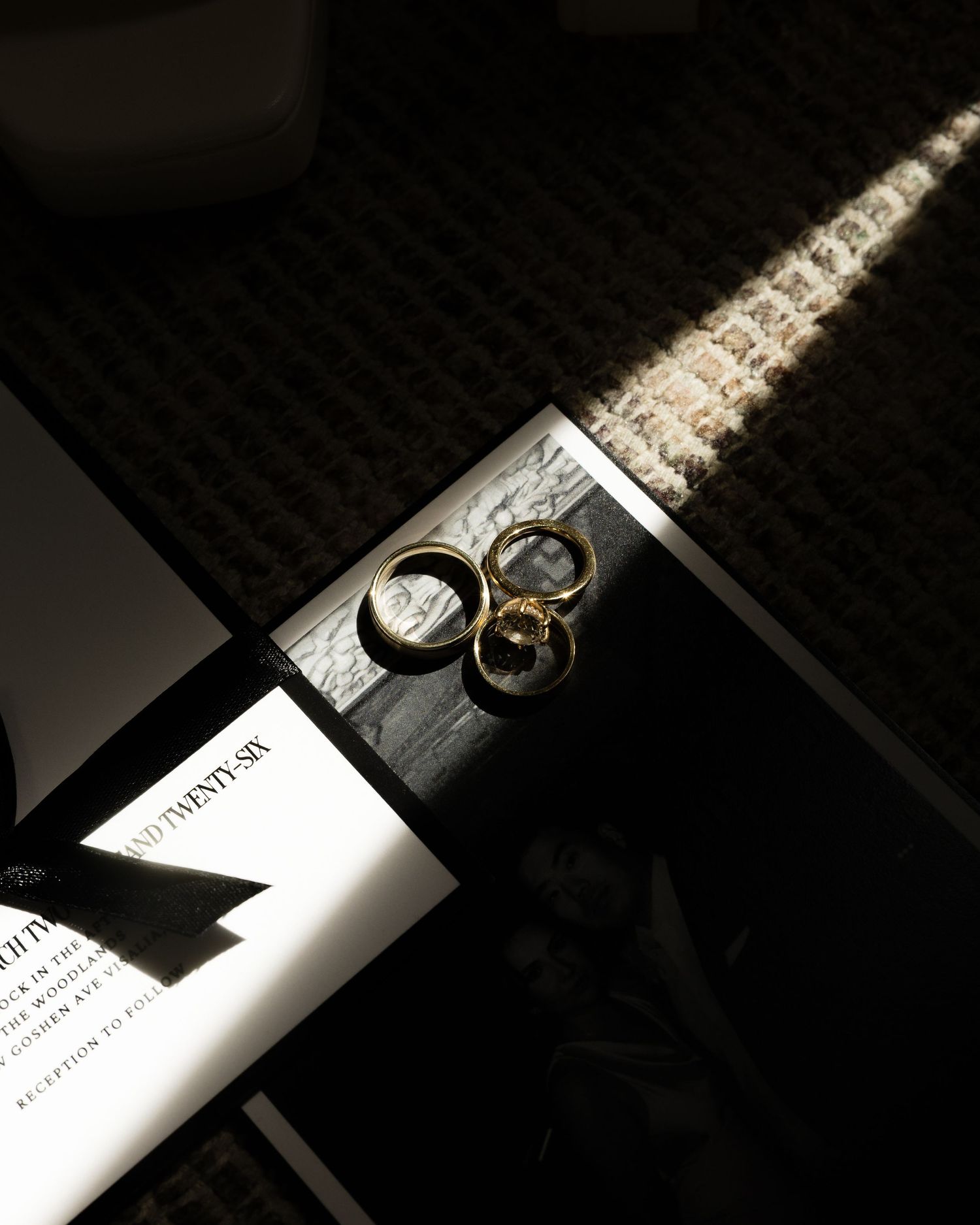 Close-up of gold wedding rings resting on black wedding invitation in dramatic moody lighting.