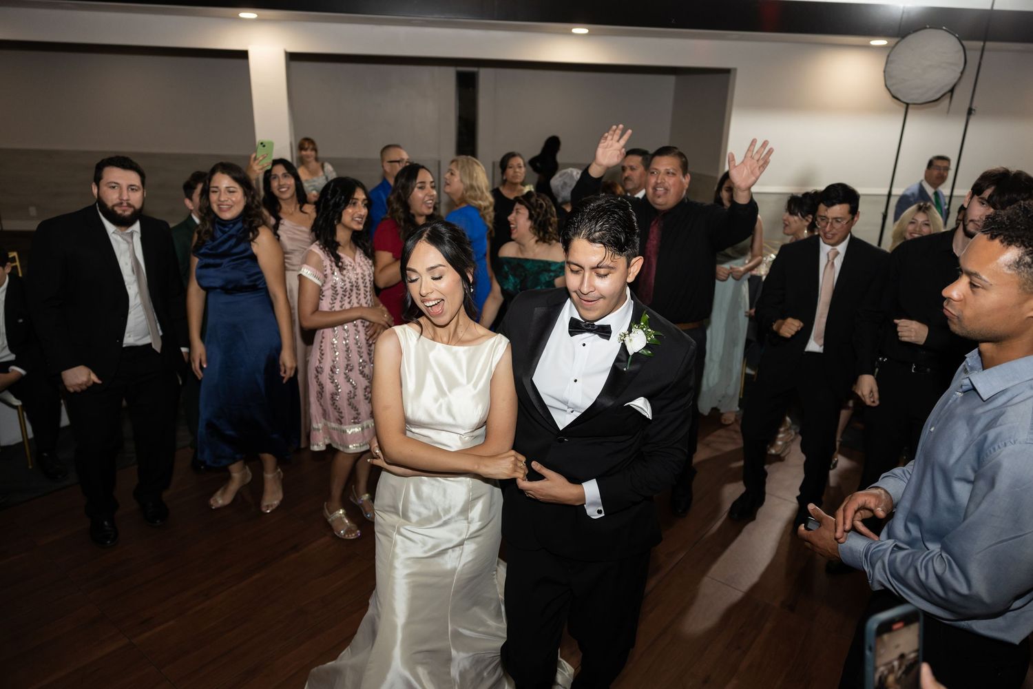 Wedding party and guests dancing energetically at an elegant indoor reception.