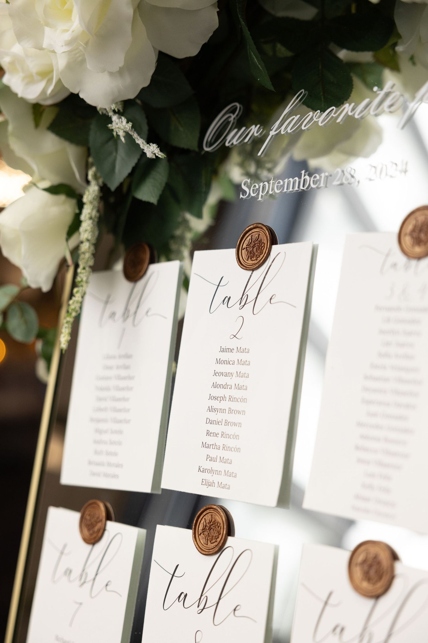 Elegant wedding seating chart with white floral decorations and wax seal table numbers.