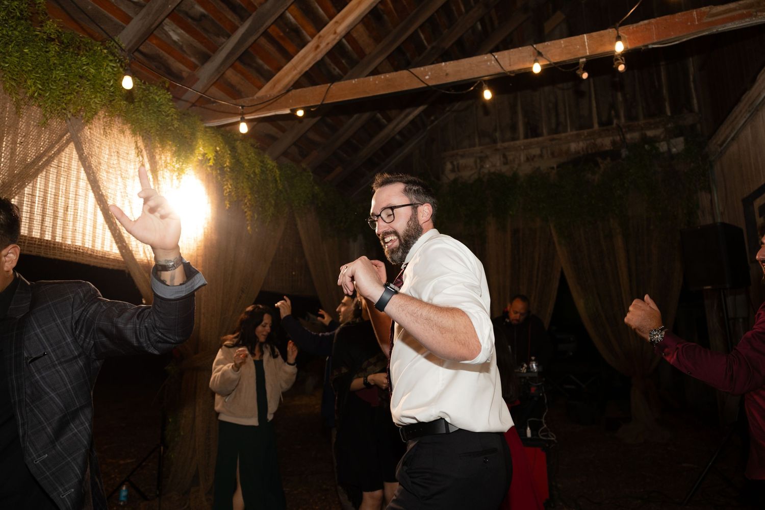 Festive wedding reception in a barn with string lights and natural decor.