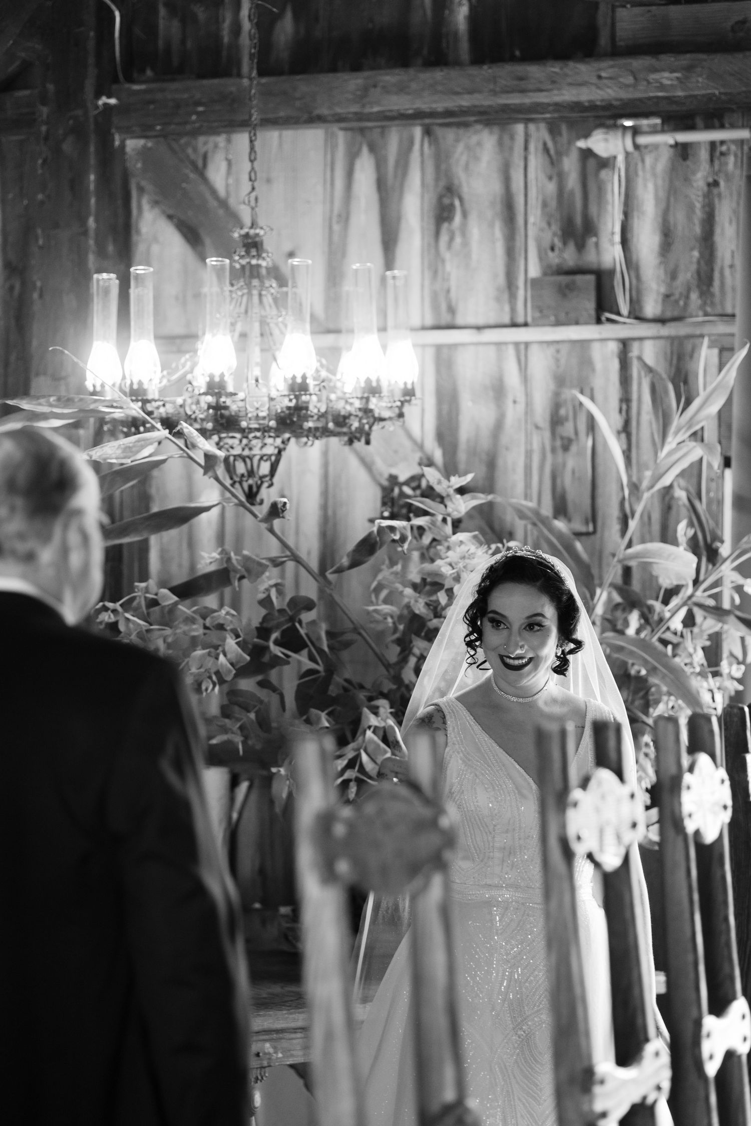 Black and white wedding photo in a rustic barn venue with elegant chandeliers and decor.