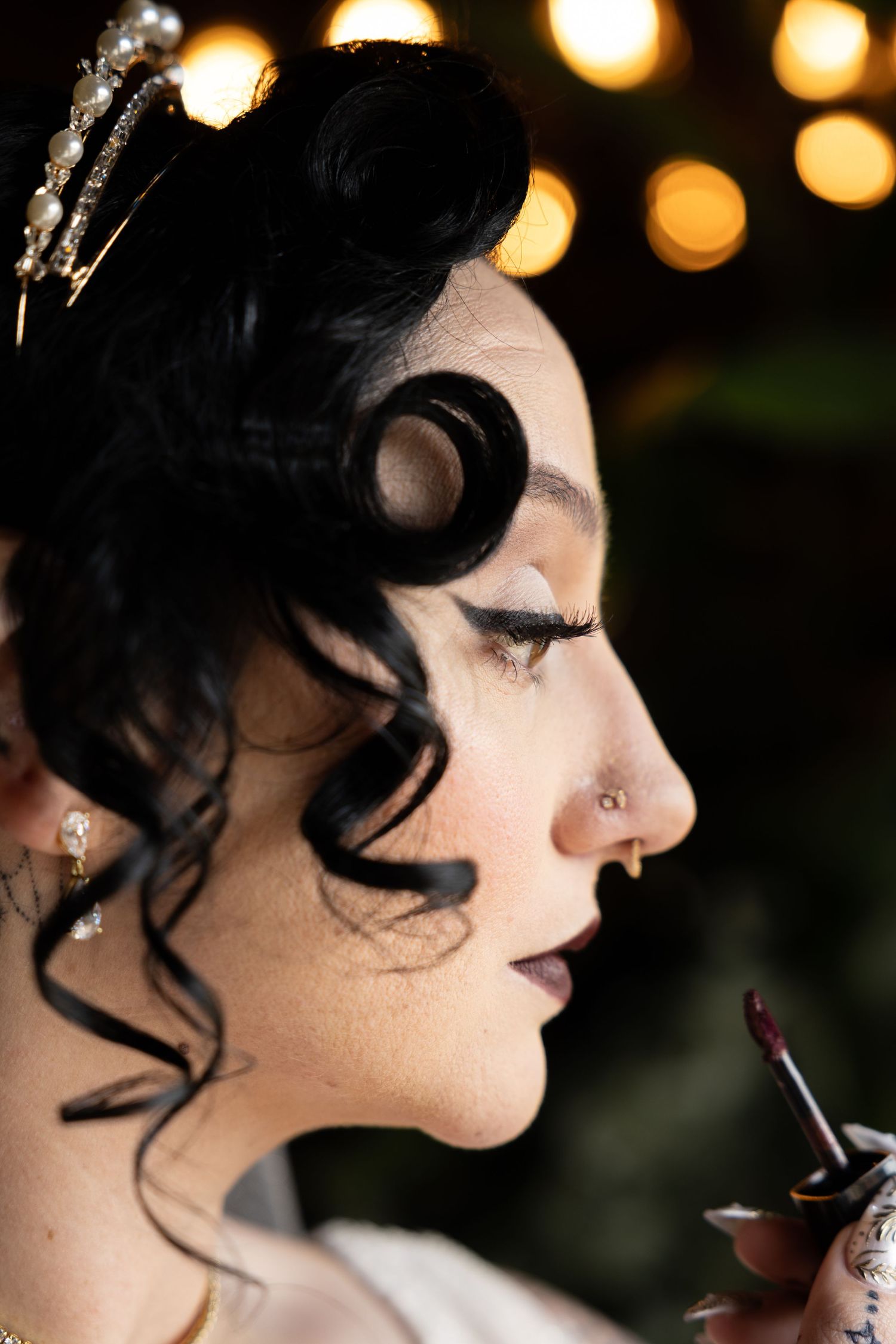Vintage-inspired bridal beauty look with pin curls and dramatic makeup against bokeh lights.