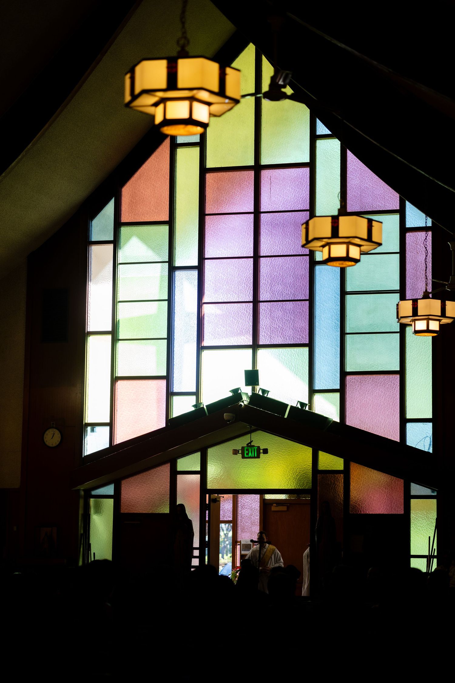 Colorful stained glass windows and pendant lights create a geometric pattern in a modern church interior.