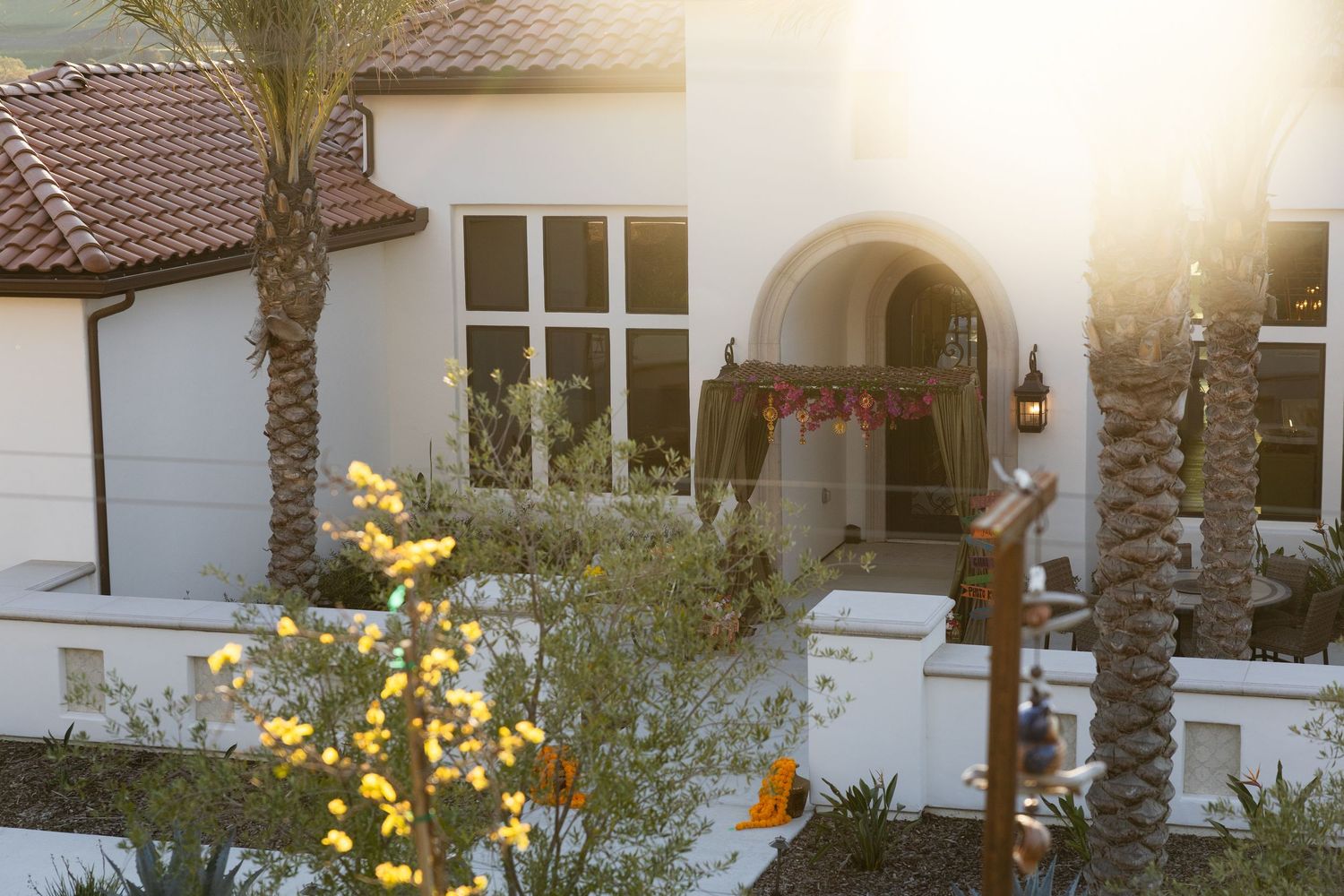 Mediterranean style villa with white stucco walls, terracotta roof tiles and palm trees in golden sunlight.