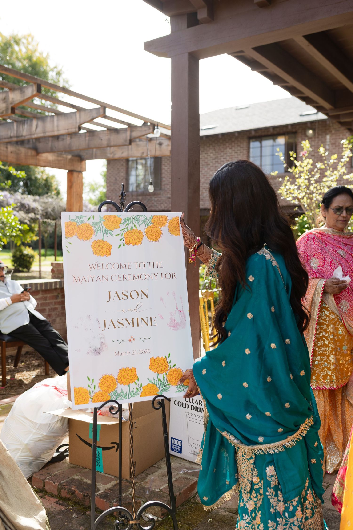Wedding reception setup with decorative signs and guests in traditional South Asian attire.