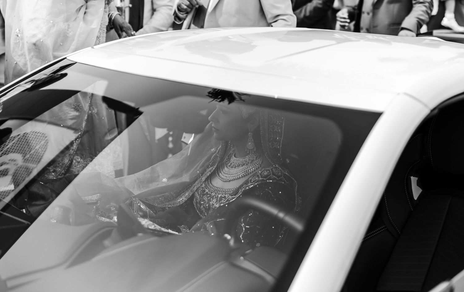Black and white photo of a couple sitting in a white car seen through the windshield.