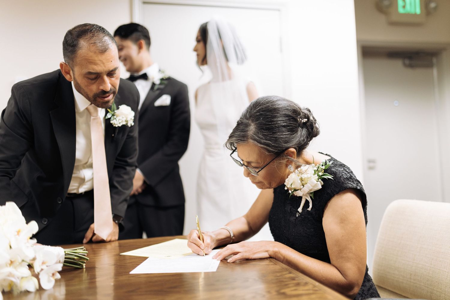 Wedding party members signing official documents at a table during the ceremony.