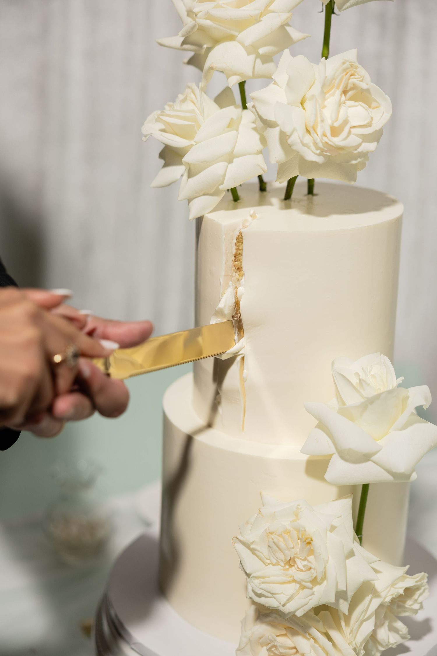Close-up details of a white wedding cake decorated with fresh roses and gold accents.