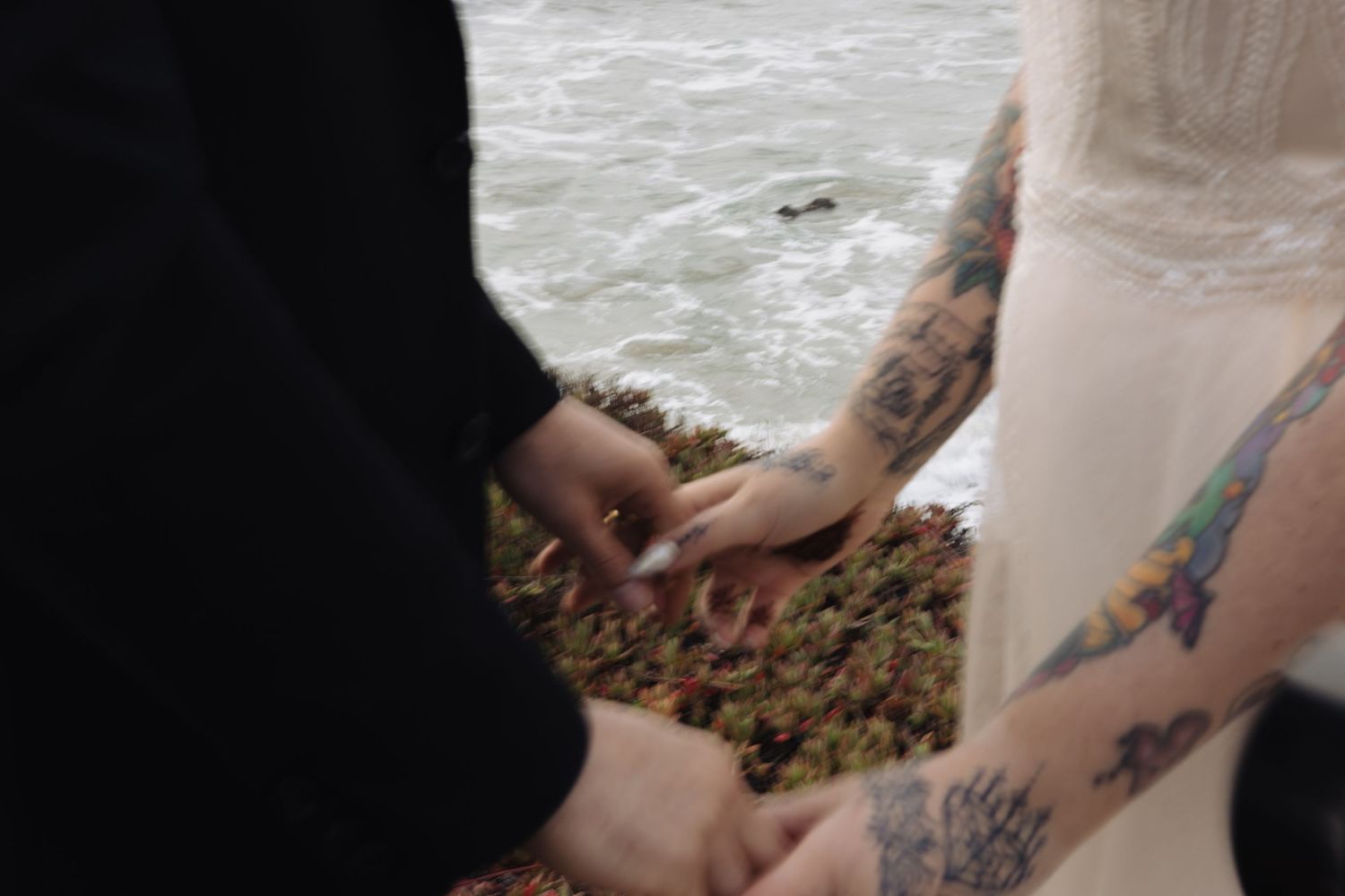 Detail shot of tattooed hands during an intimate coastal wedding ceremony.