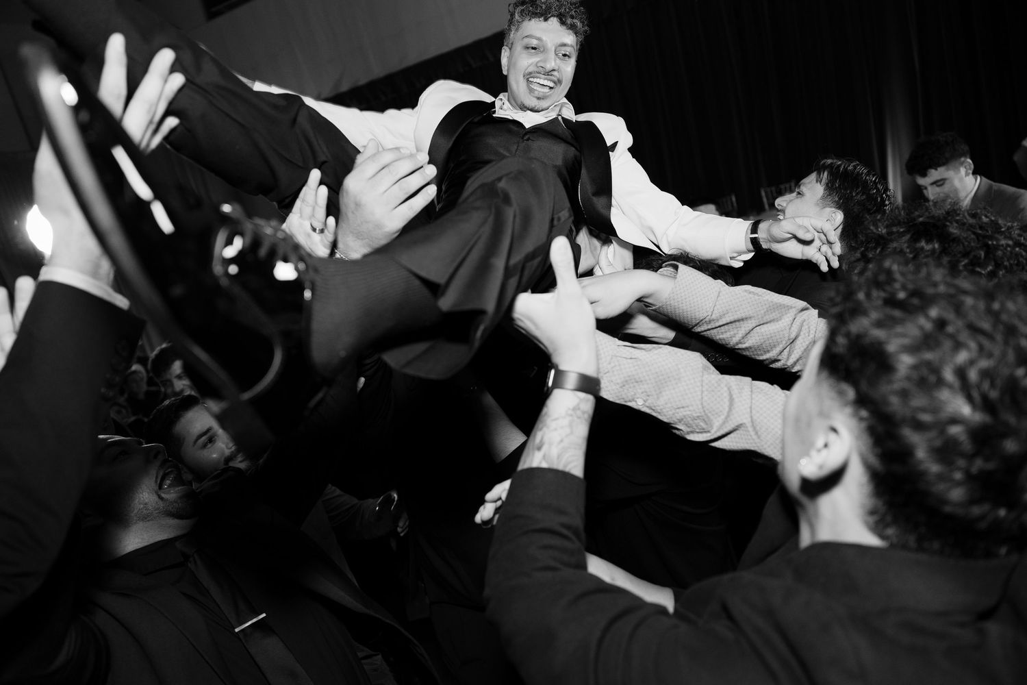 Dramatic black and white shot of wedding guest being lifted by crowd.