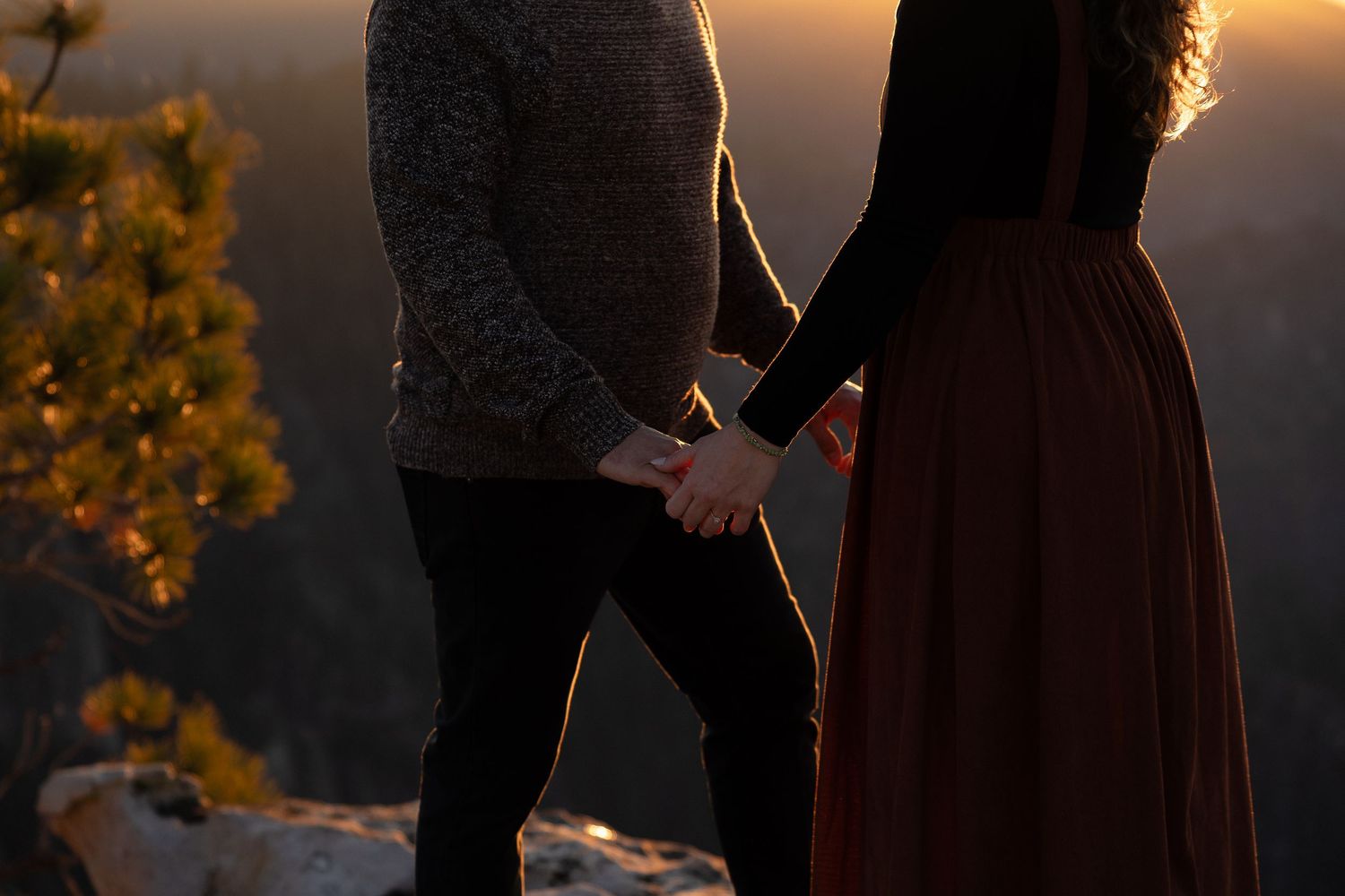 A romantic couple embraces on a mountaintop during golden hour sunset.