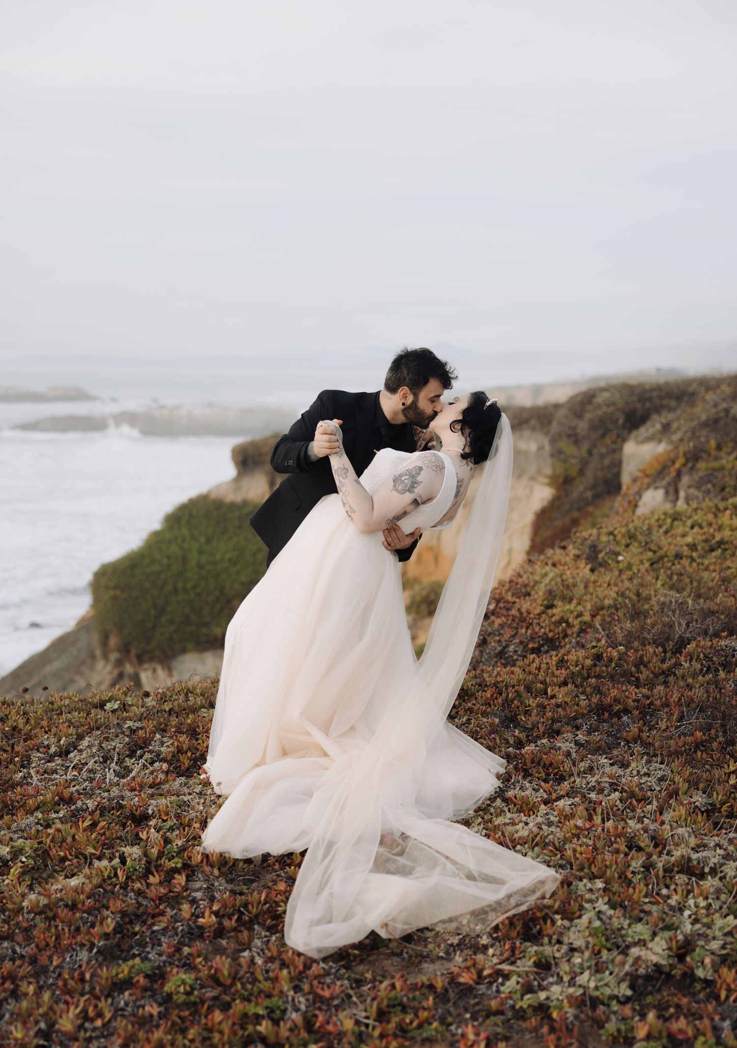 A couple shares an intimate moment on a coastal cliff covered in autumn foliage.
