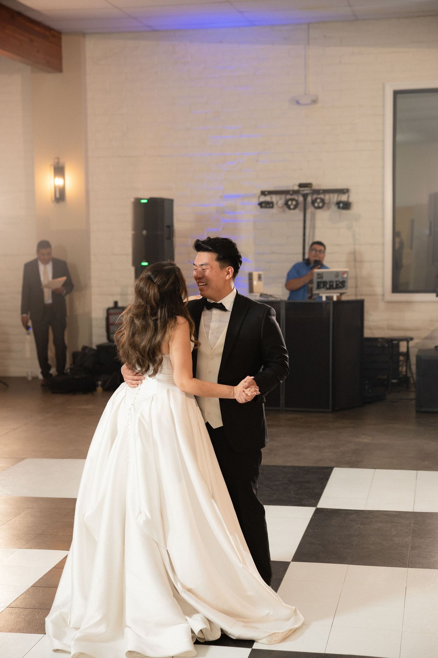 Bride and groom share their first dance on a checkered dance floor at an elegant wedding reception.