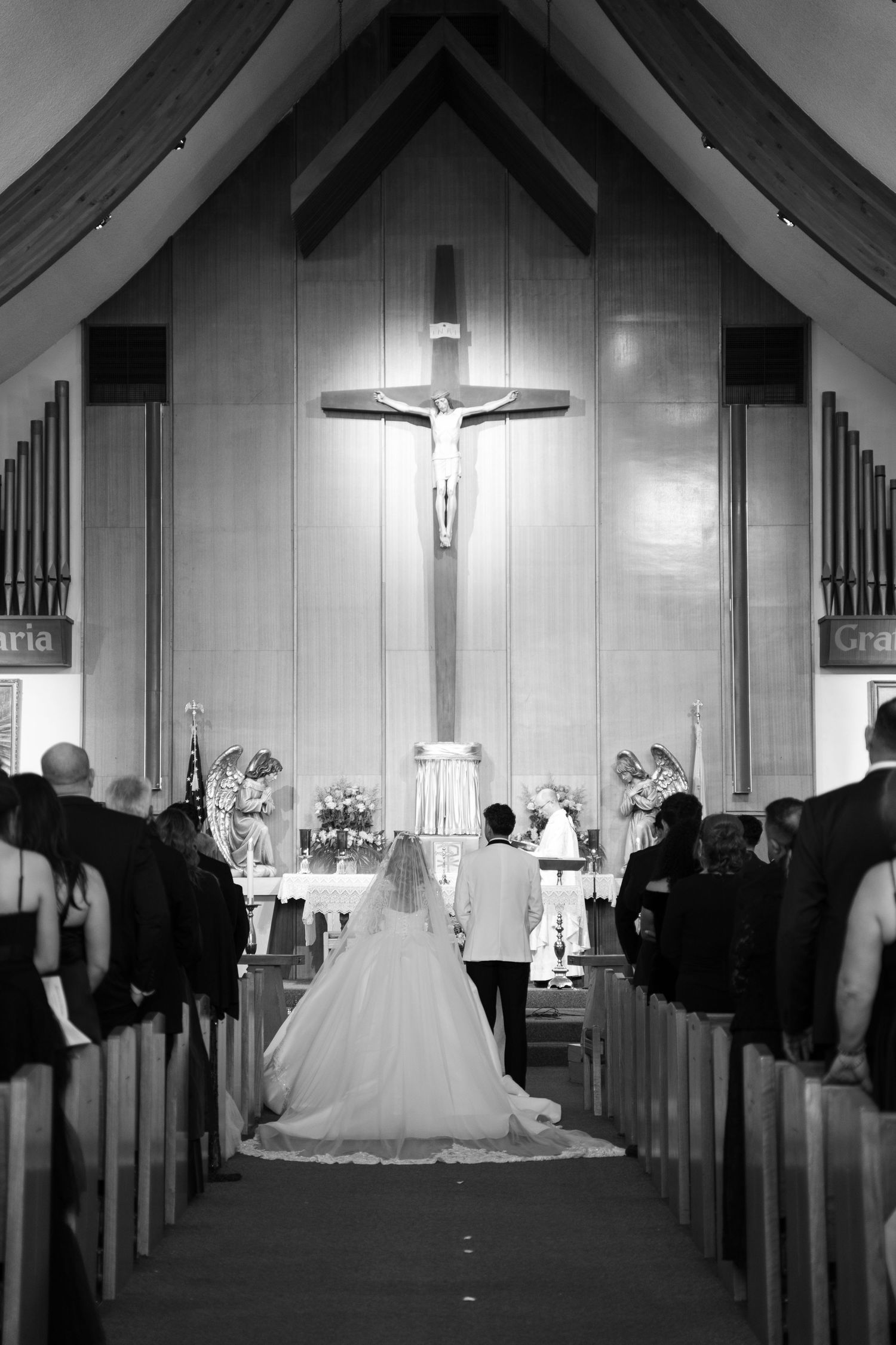 A dramatic black and white church wedding photo showing a bride and crucifix at the altar.