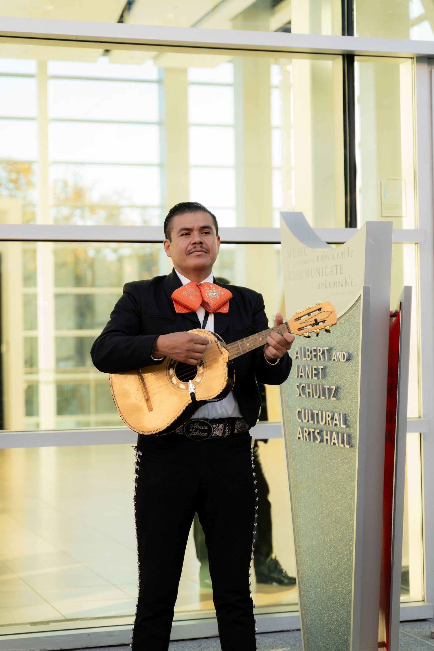 A mariachi band in traditional black suits performs with string instruments in a bright indoor space.