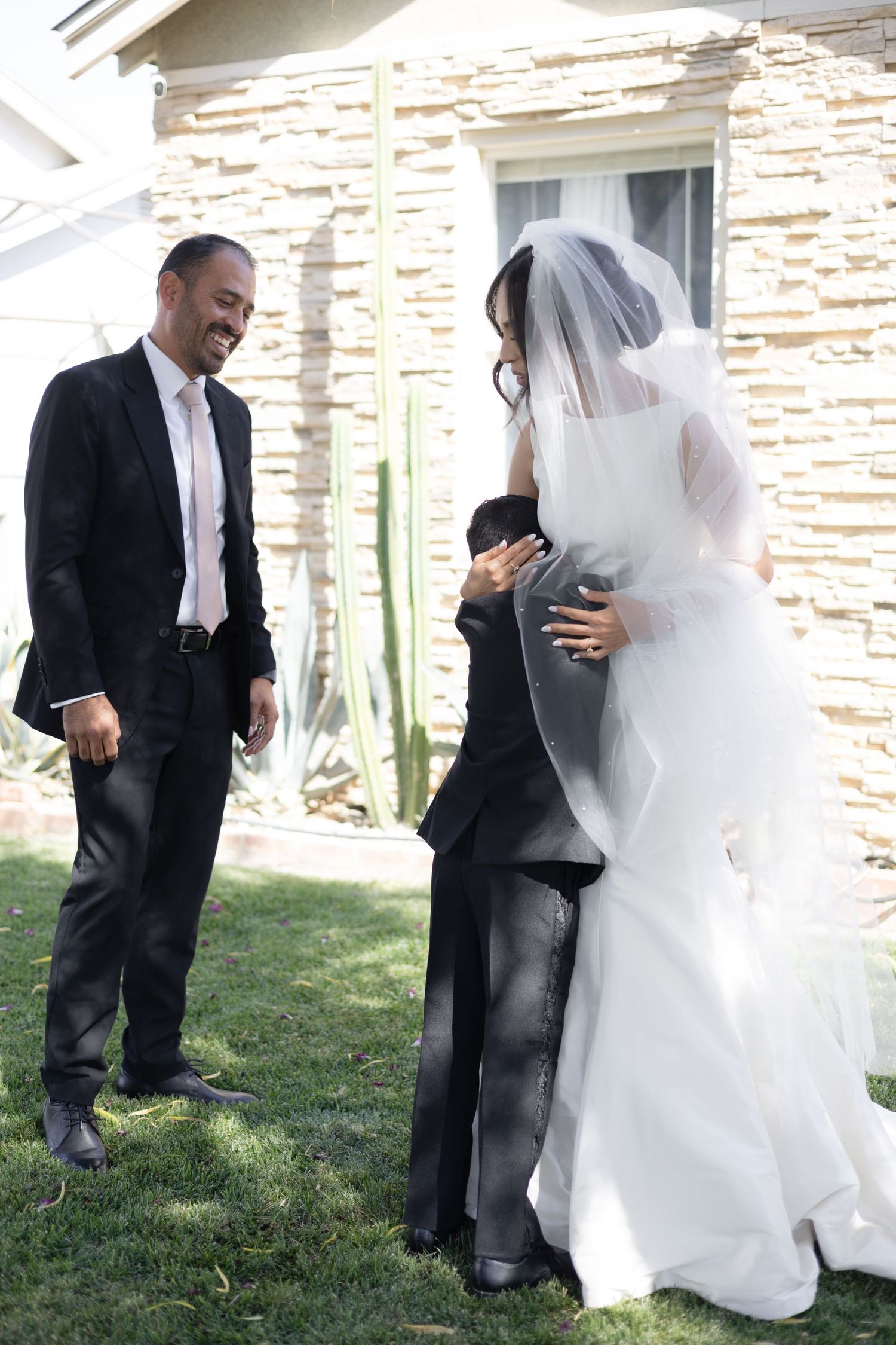 Wedding party members in formal attire share a moment outside a stone building.