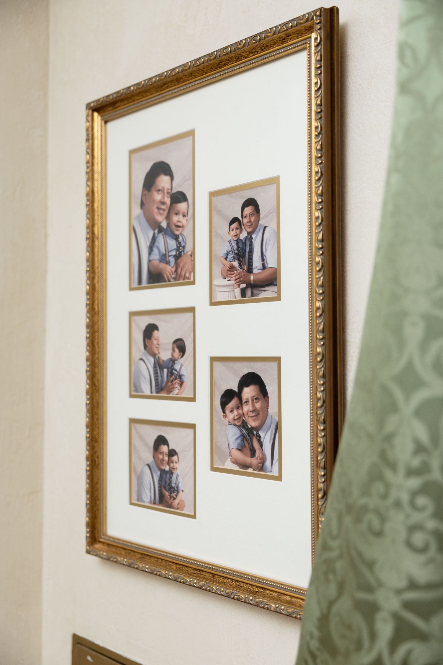 A wall gallery display featuring multiple family portraits in ornate gold frames against a light colored wall.