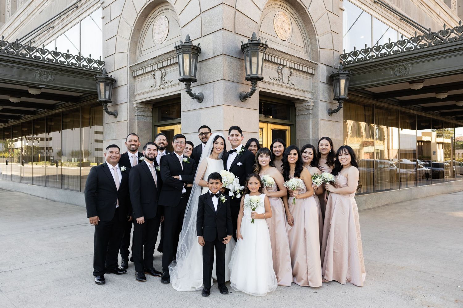Wedding party members arranged in formal poses outside historic building entrance.