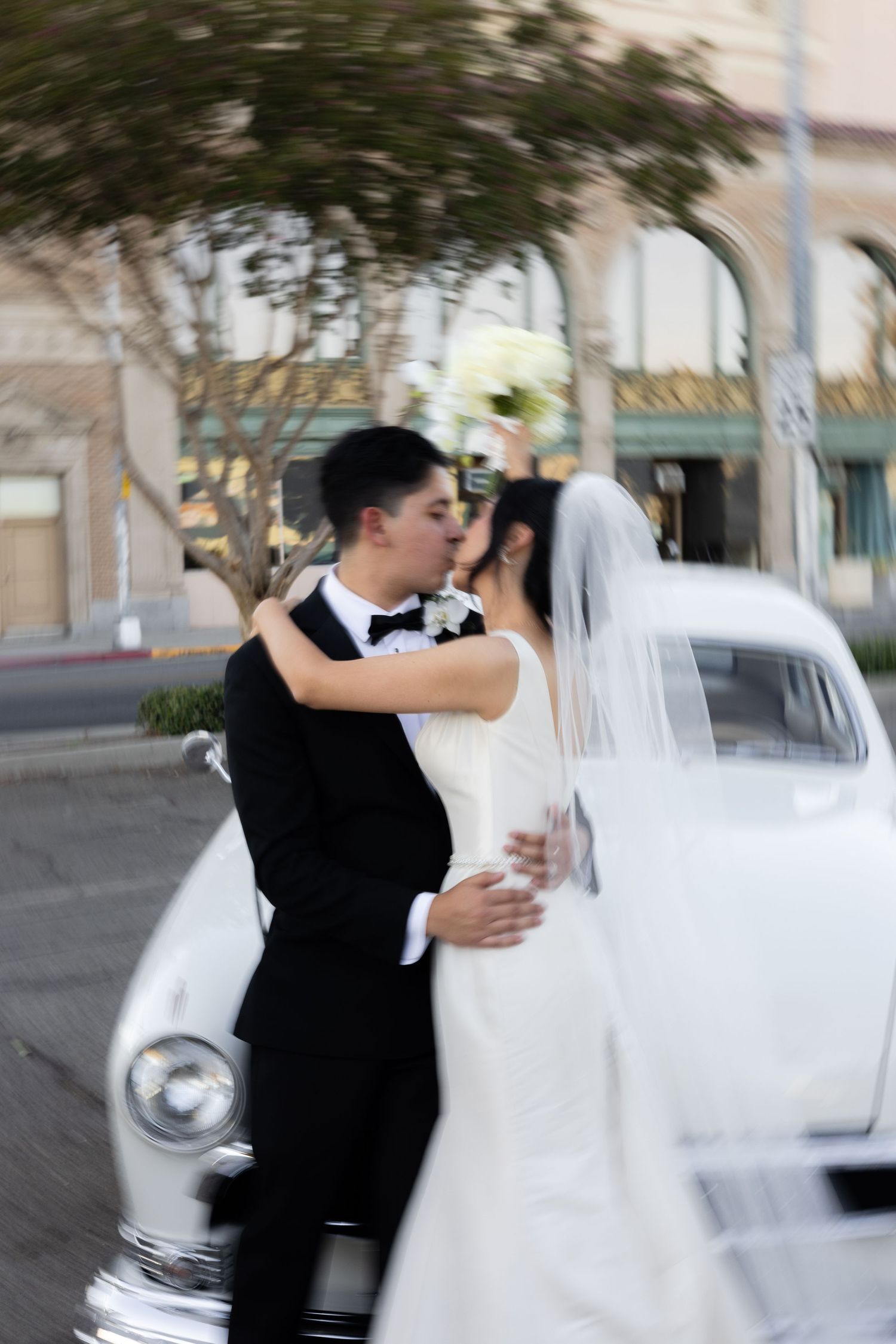 Dancing newlyweds share intimate moment beside vintage car.
