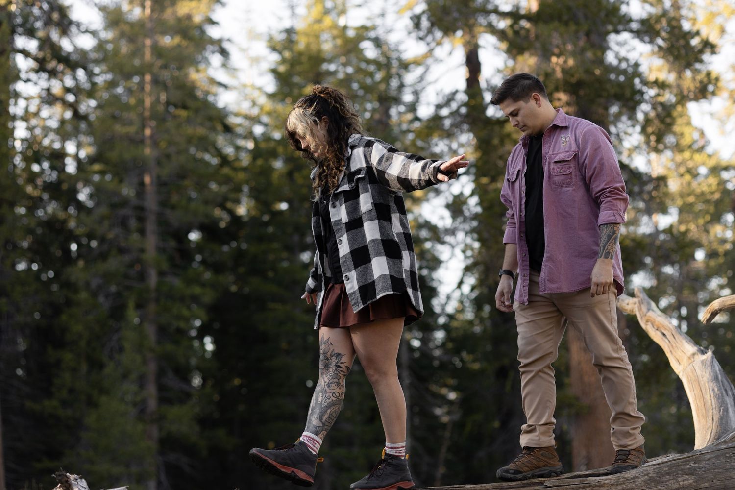 Couple balancing on fallen tree trunk in forest during adventure session.